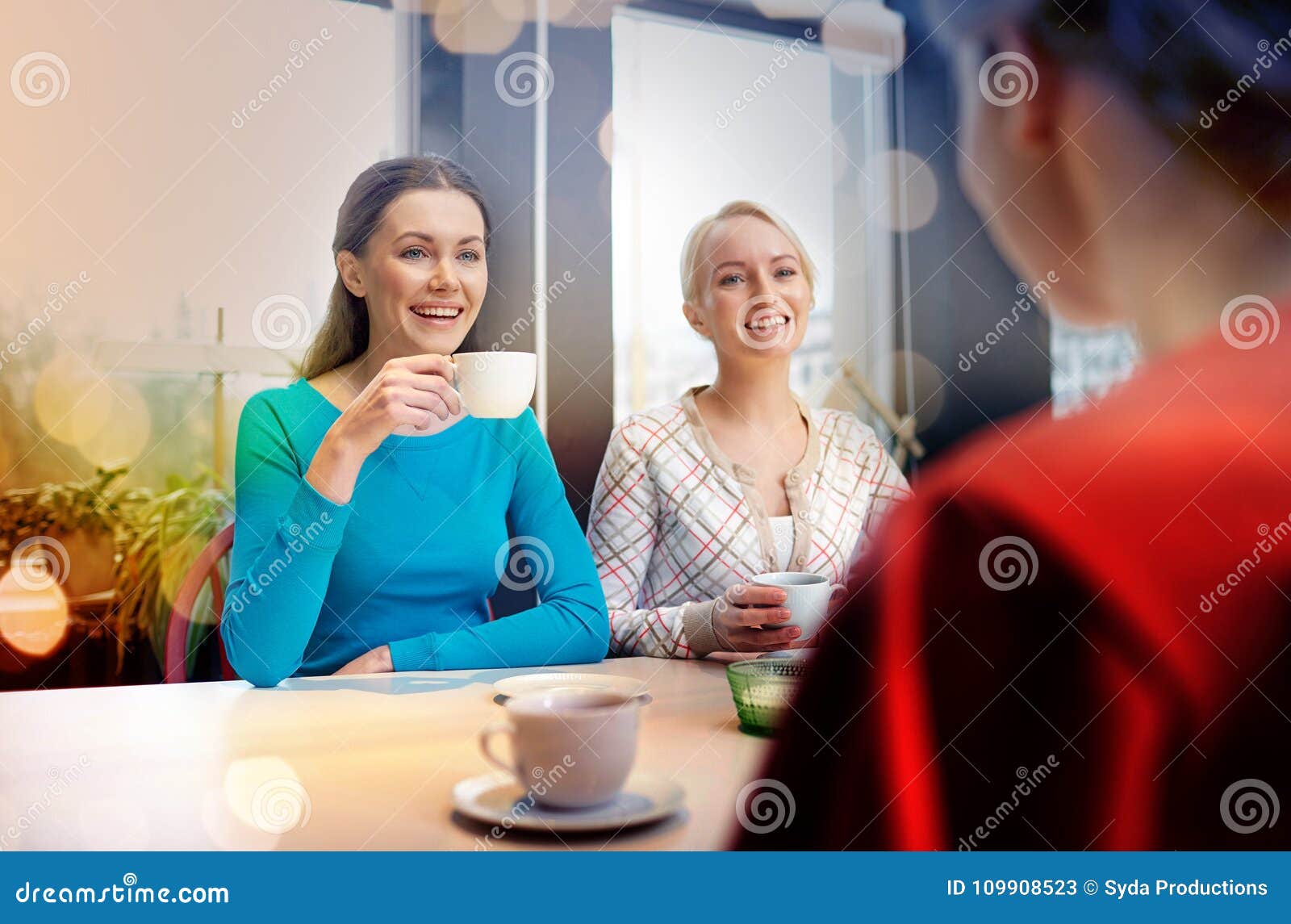 Happy young women drinking tea or coffee at cafe. People, leisure, friendship and communication concept - happy young women meeting and drinking tea or coffee at cafe