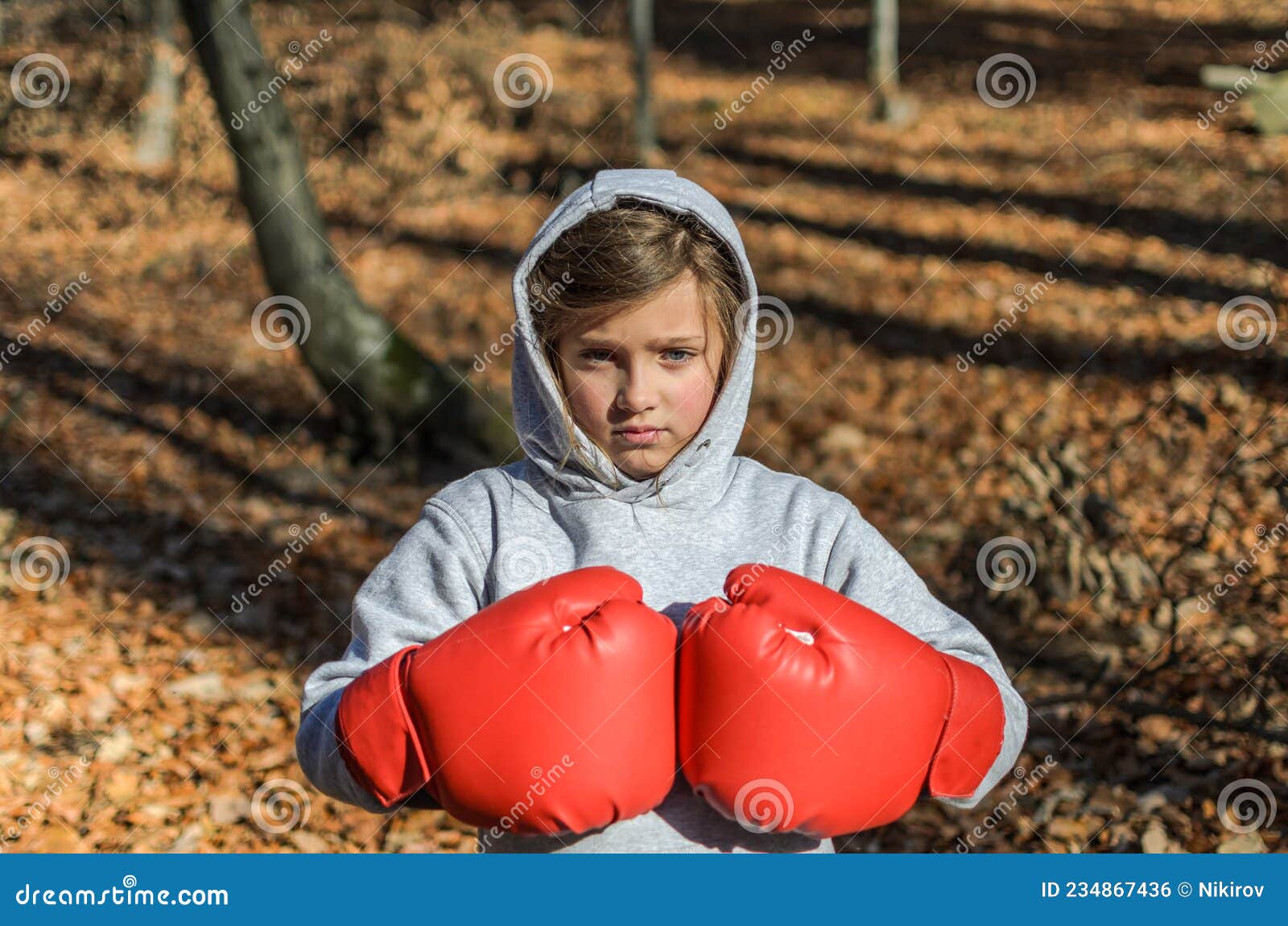 Pequeña Adorable Niña En Un Traje De Chándal Con Una Capucha En La Cabeza  Con Guantes De Boxeo Rojo Boxeando En La Calle En El Fre Foto de archivo -  Imagen de