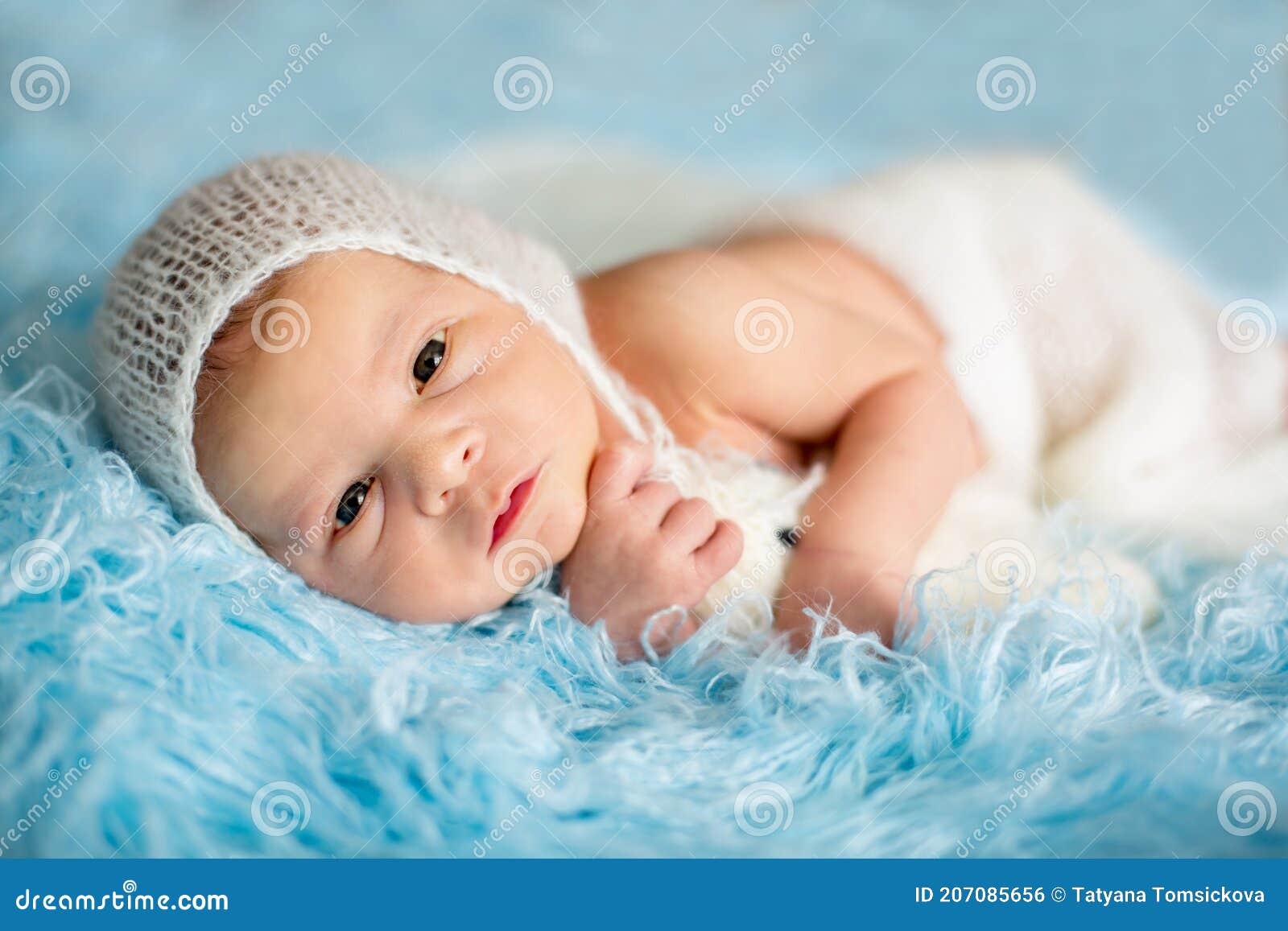 Un lindo bebé recién nacido con ropa ligera está jugando con juguetes  educativos tirados en el suelo sobre una manta de lino gris. vista  superior. productos para niños. feliz infancia y maternidad.
