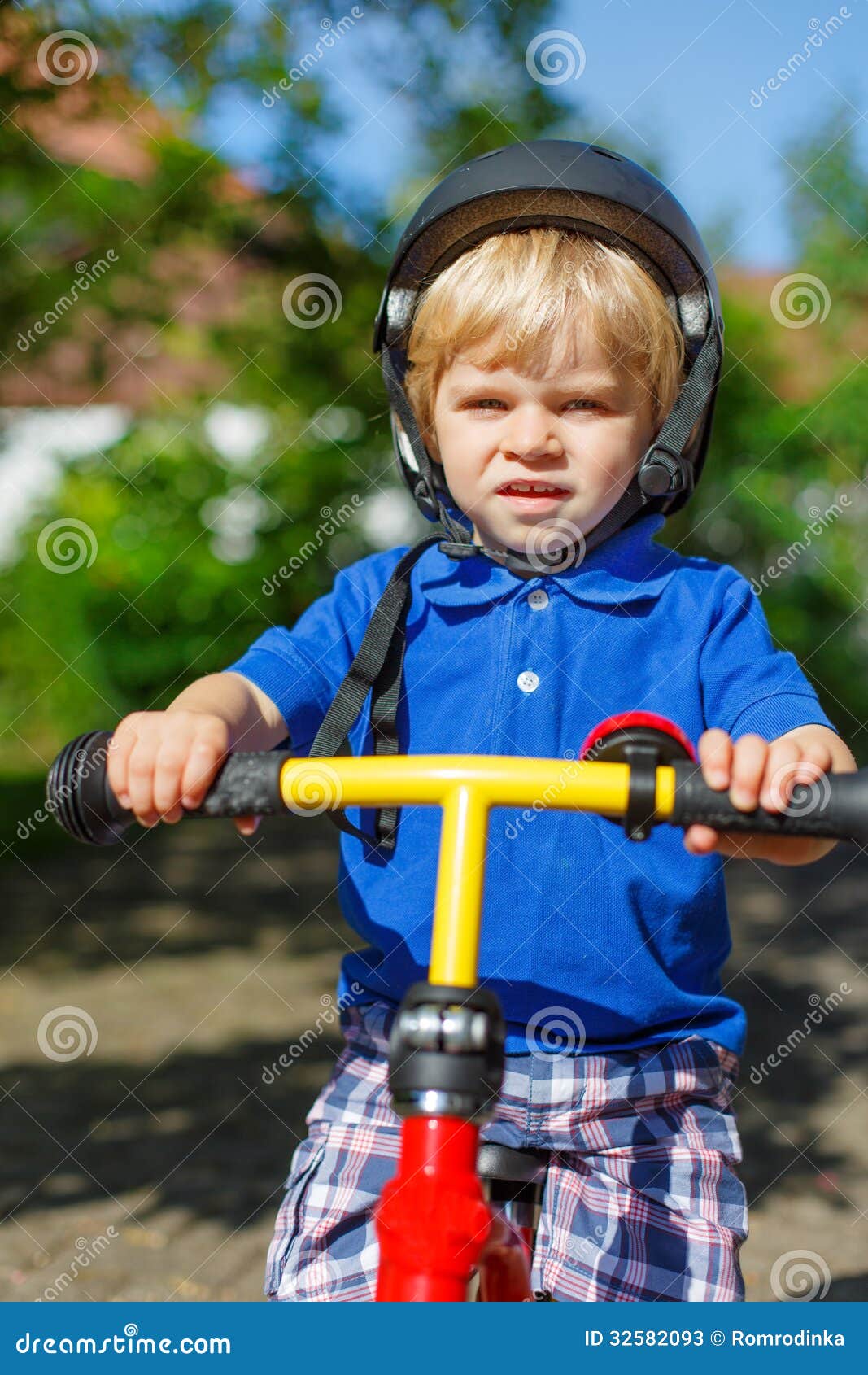 Pequeño montar a caballo del niño pequeño en su bycicle en verano. Pequeño niño pequeño en el montar a caballo del casco de seguridad en su bycicle en jardín del verano