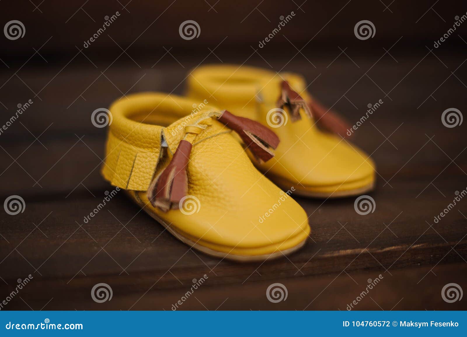 Pequeños zapatos amarillos lindos del niño con el cordón marrón en el fondo marrón borroso del piso