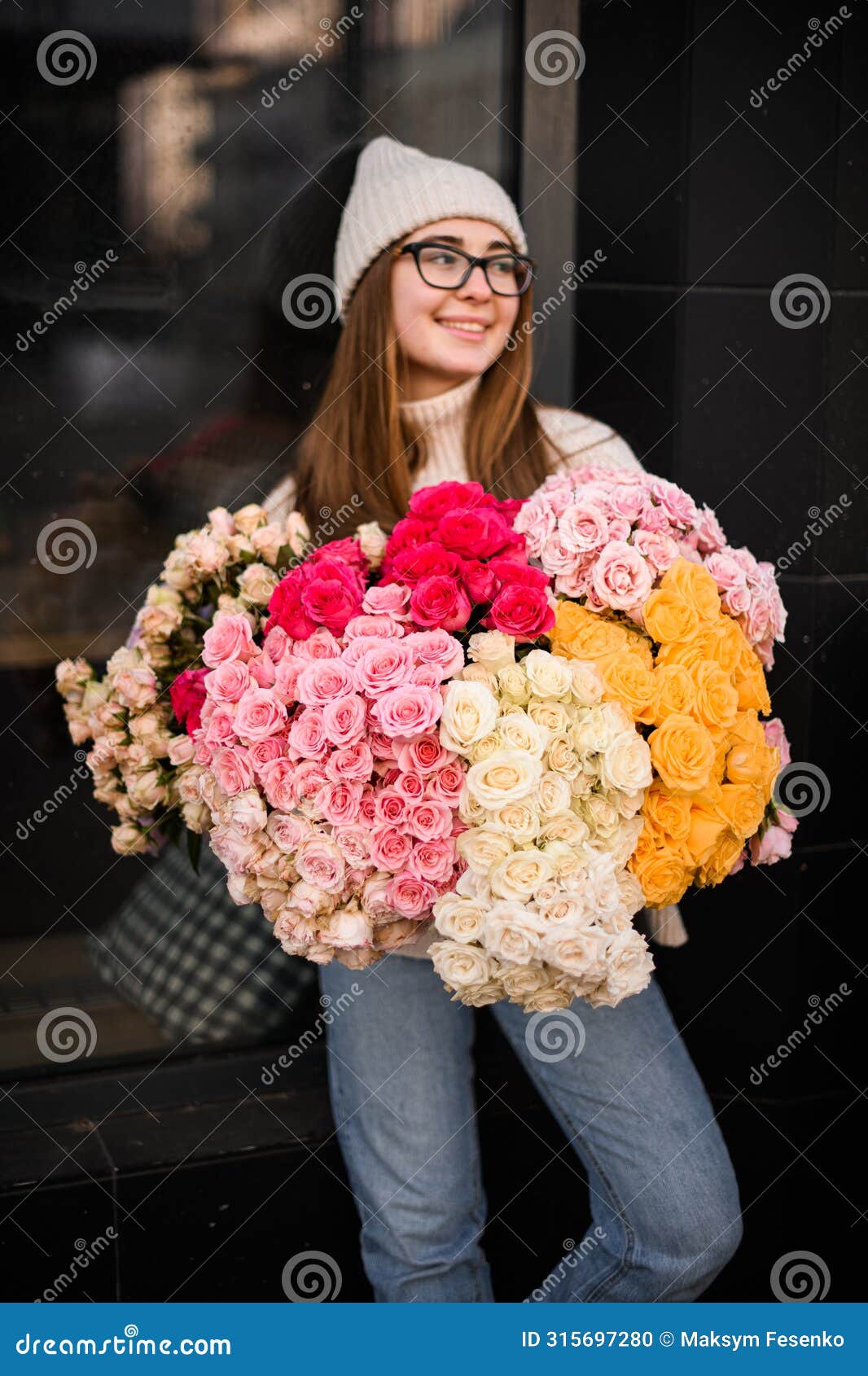 perky girl in light sweater and jeans stands with a bouquet of colorful flowers