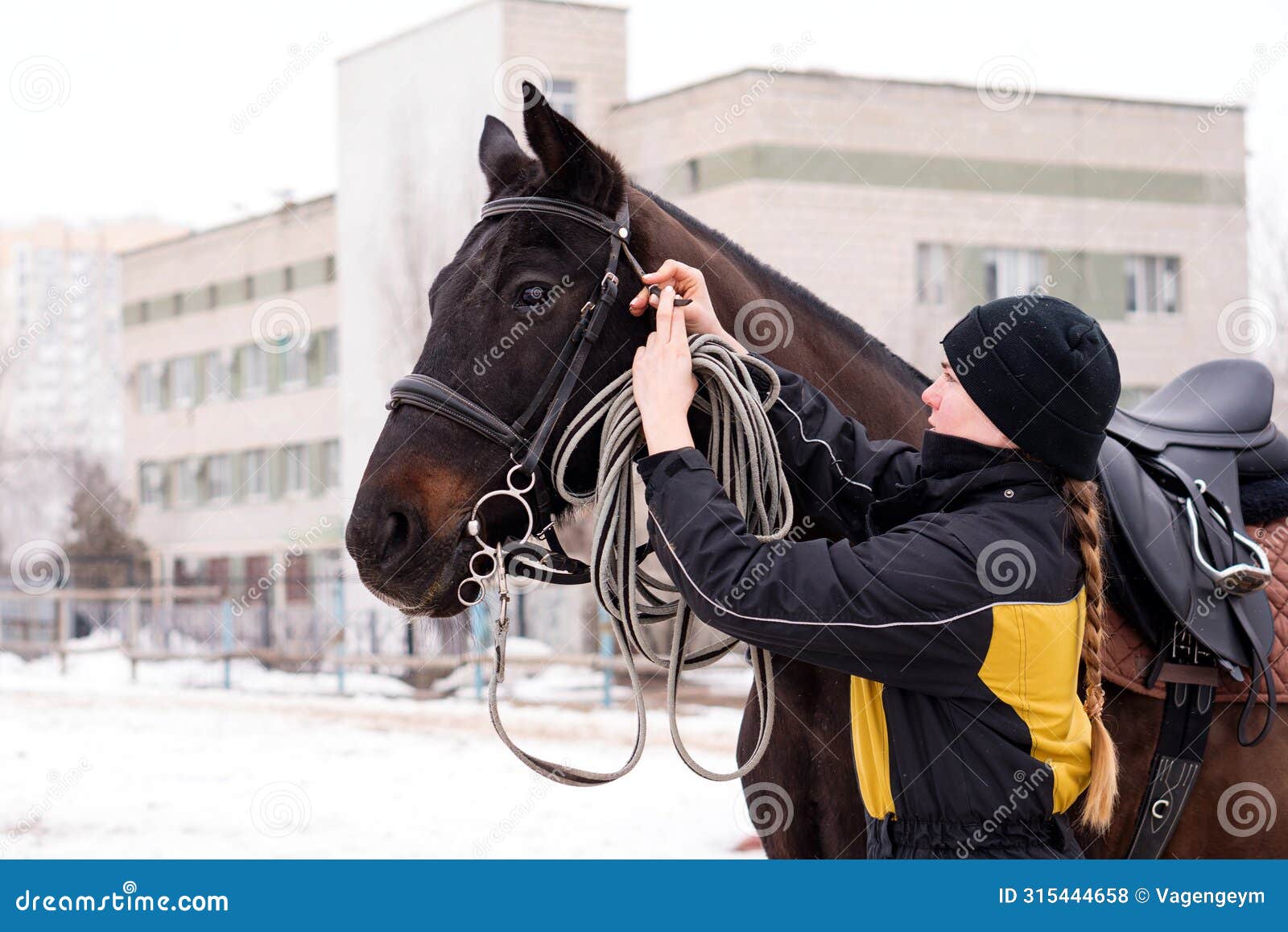 person adjusting reins on saddled horse outdoors