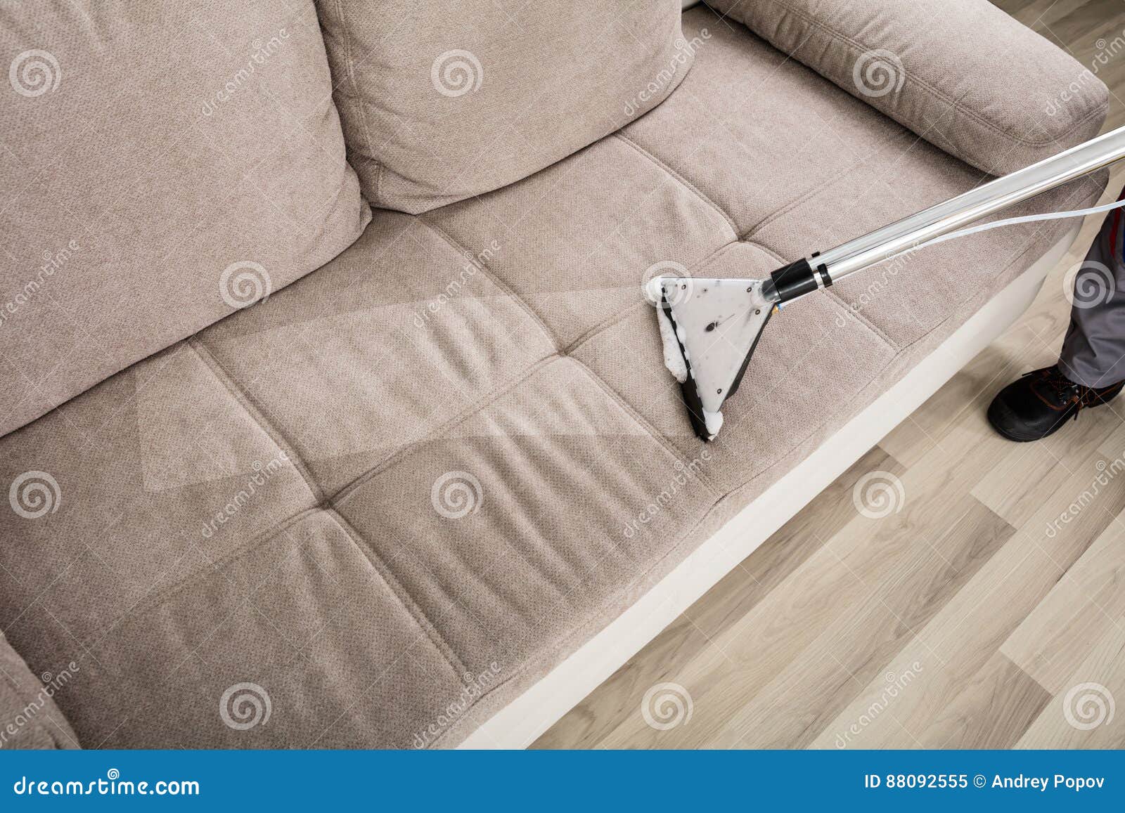 person cleaning sofa with vacuum cleaner