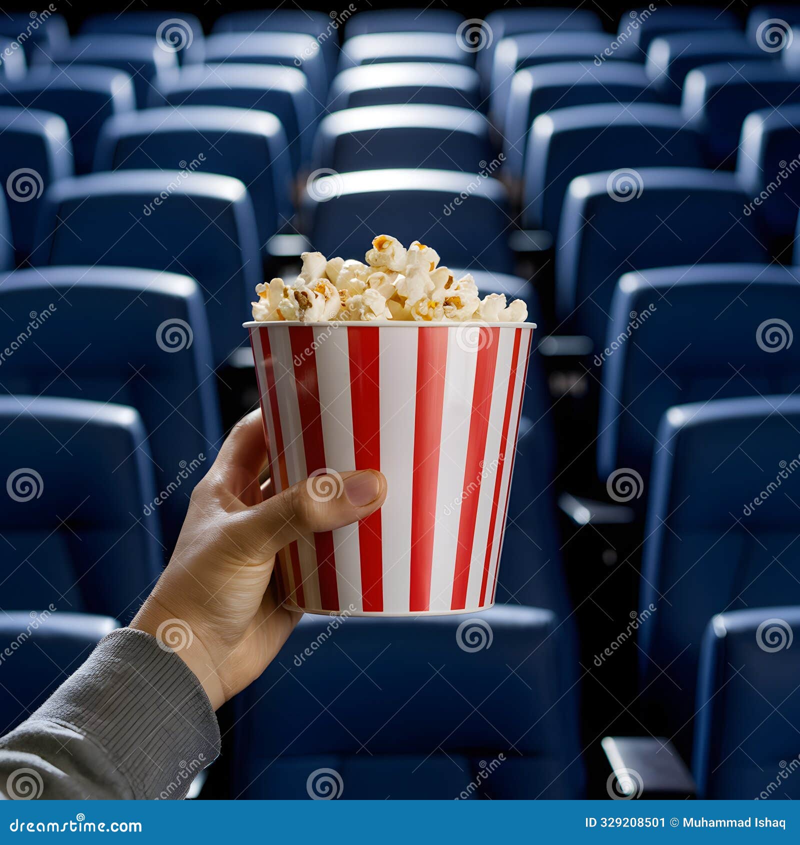 person holding red and white popcorn container in empty movie theater