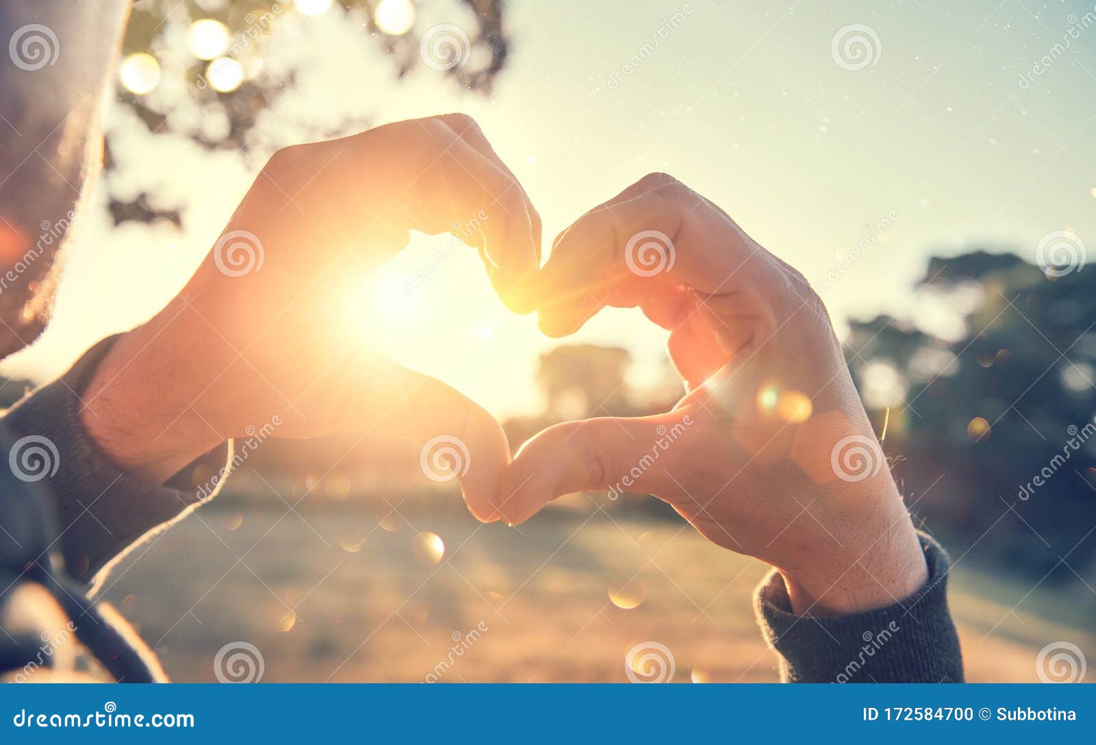 person making heart with hands over nature sunset background. happy young people. silhouette hand in heart  with sun inside