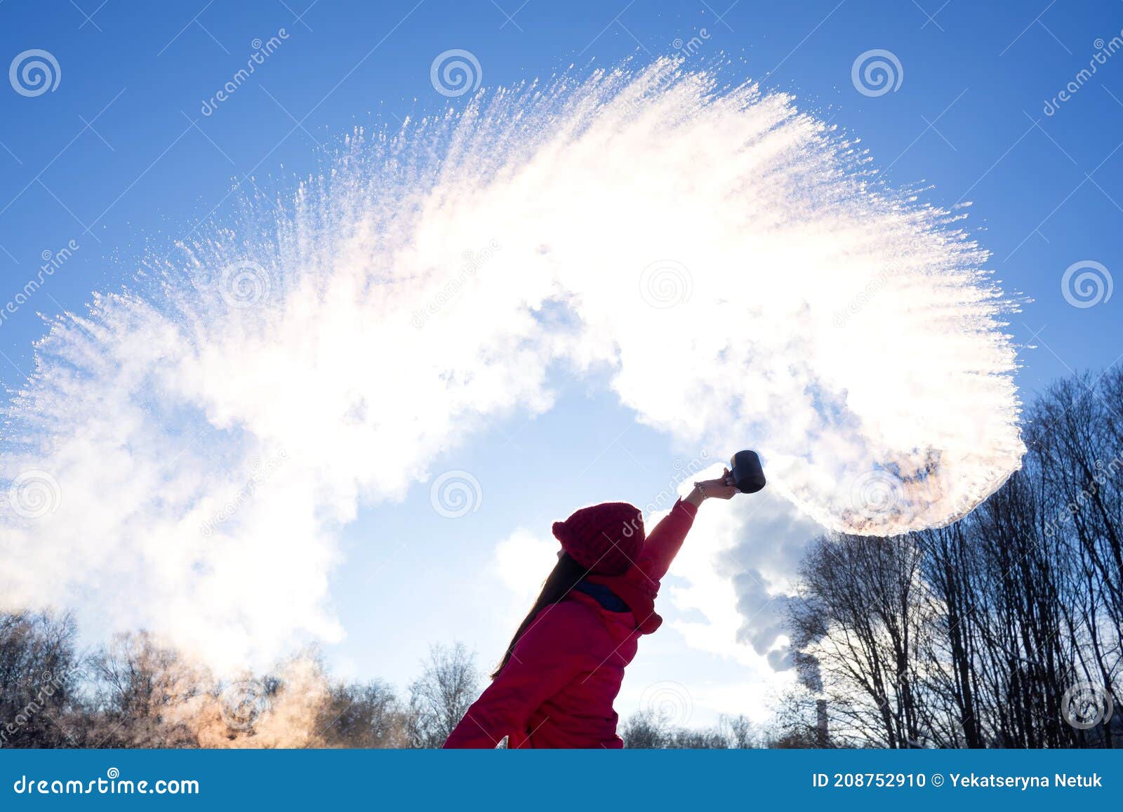 person pouring hot water up in the sky  sunny winter day. boiling water challenge  which instantly freezes  turns into snow if the