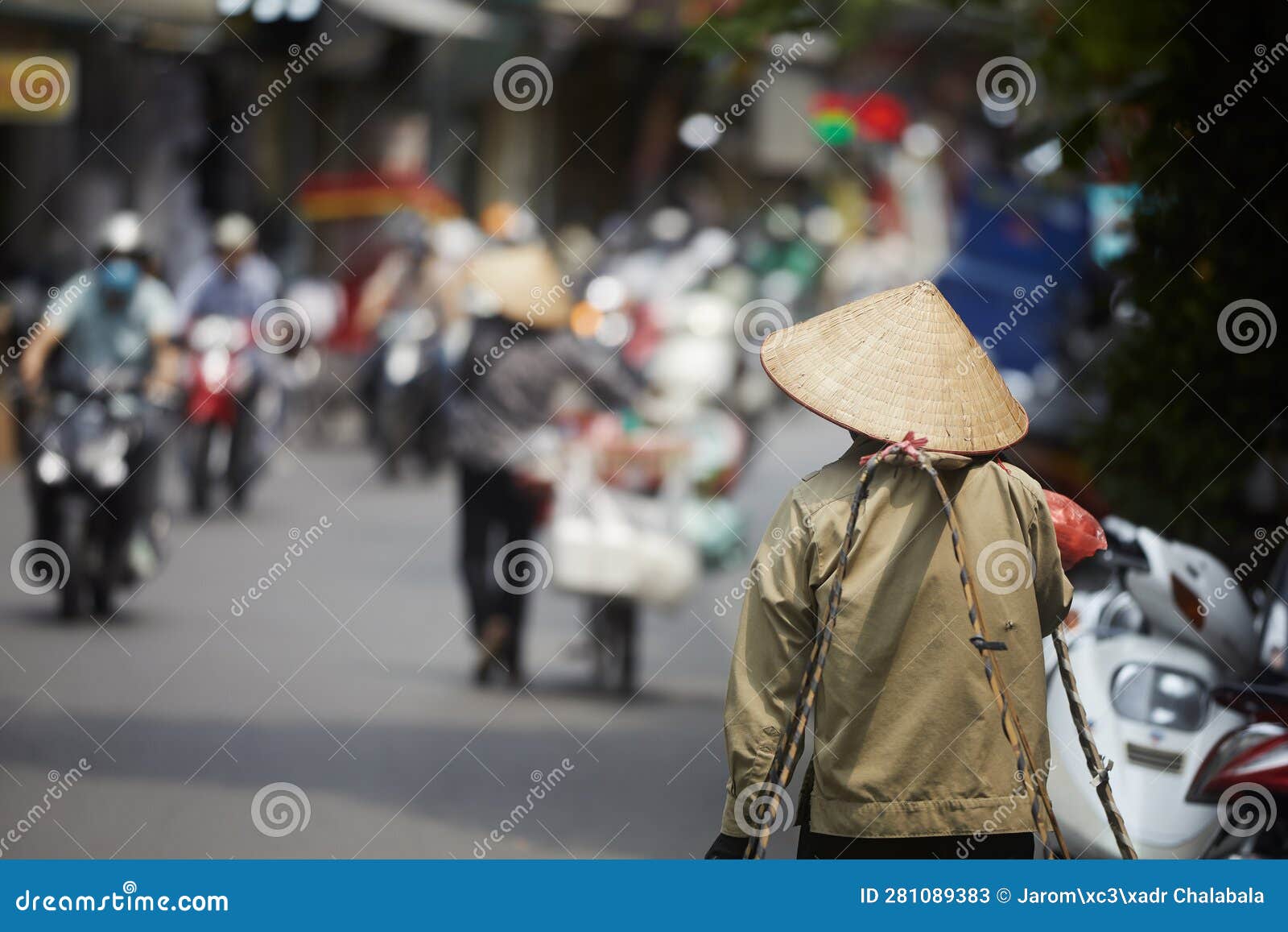 person with traditional conical hat against traffic motorbikes on busy street