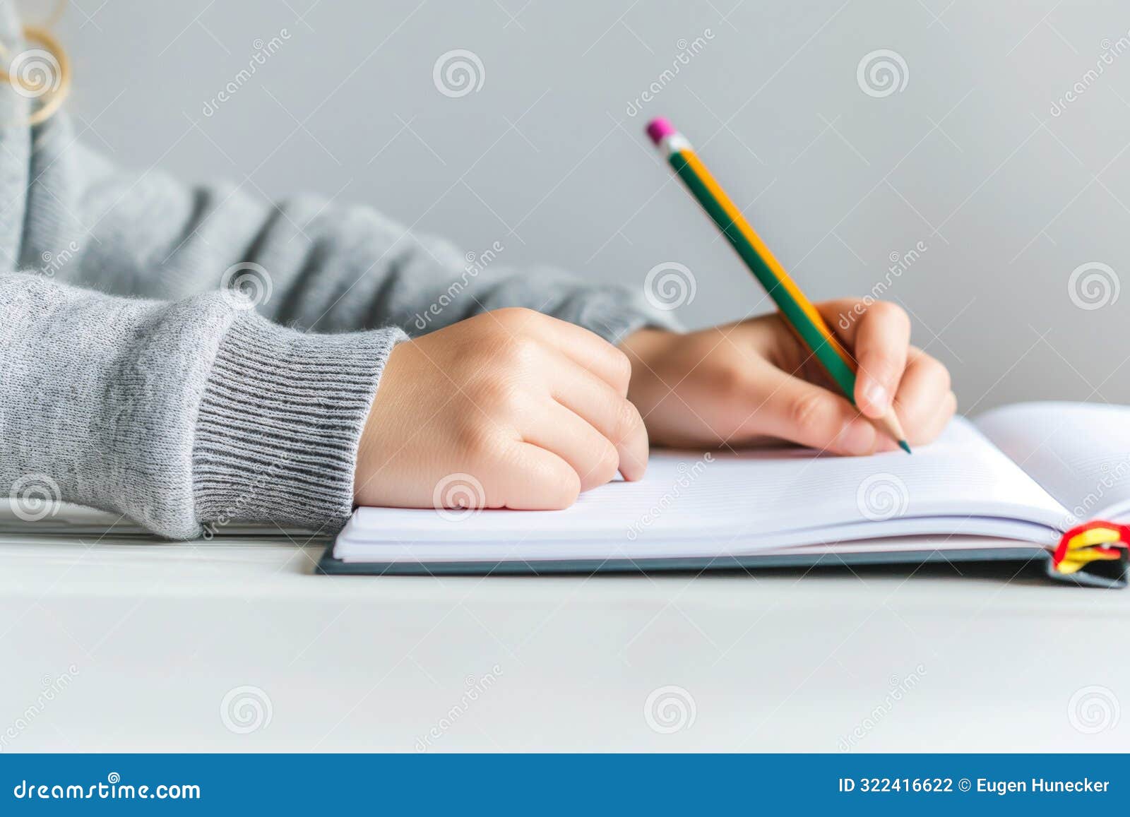 observing a closeup of hands using a pencil to write in a notebook on a white desk