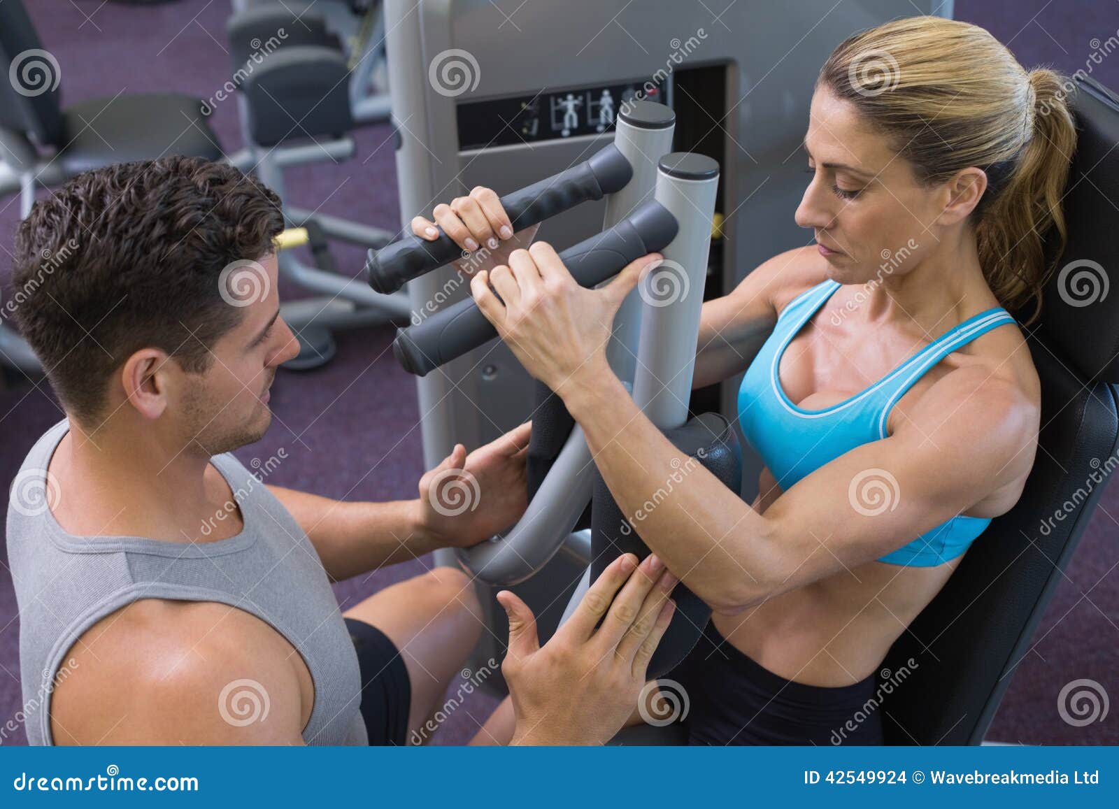 Personal Trainer Coaching Female Bodybuilder Using Weight Machine Stock