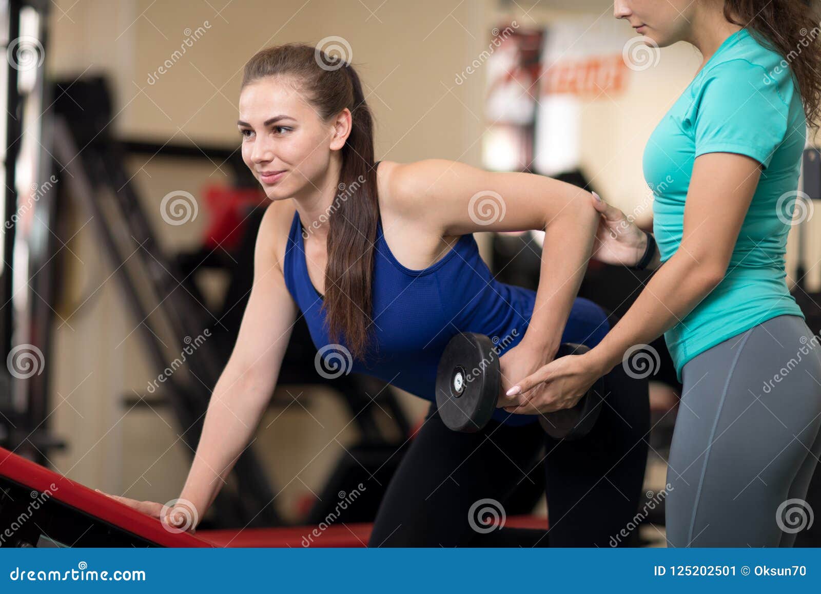 personal trainer helping woman with weight training equipment in gym