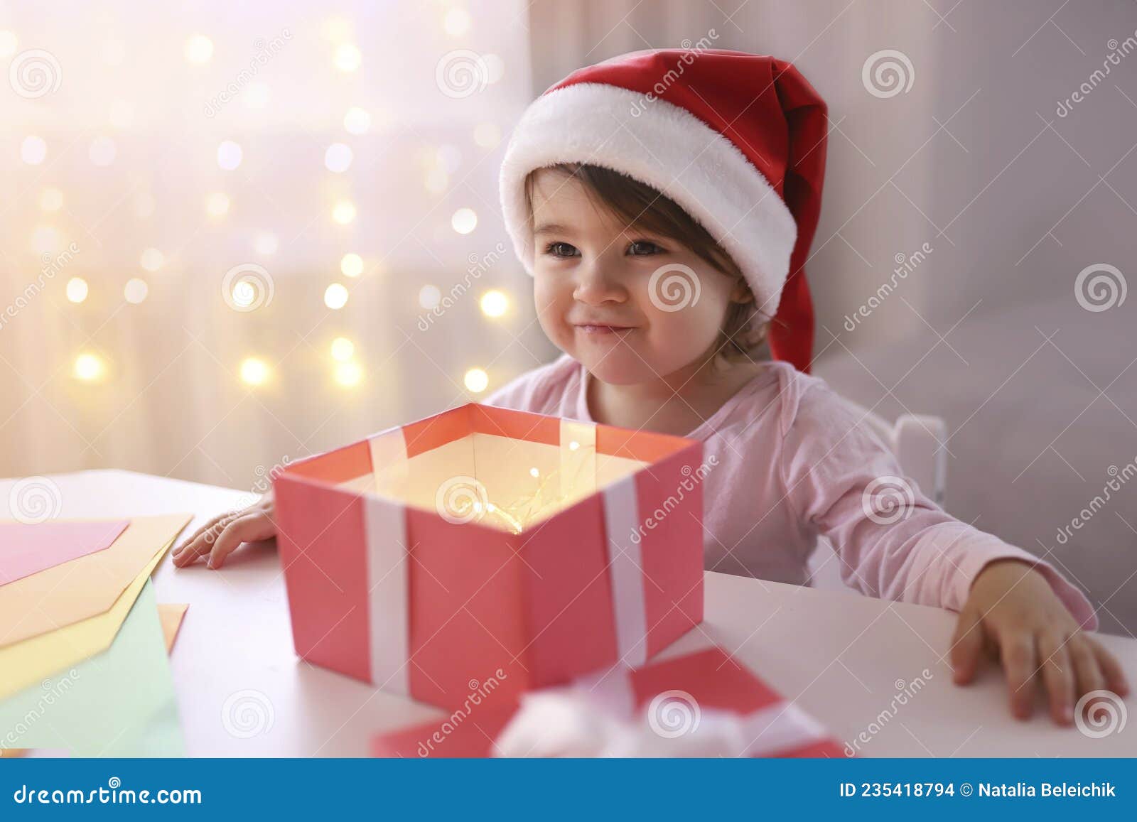 Petite Fille De Noël Dans Un Chapeau Santa Regarde Dans Une Boîte