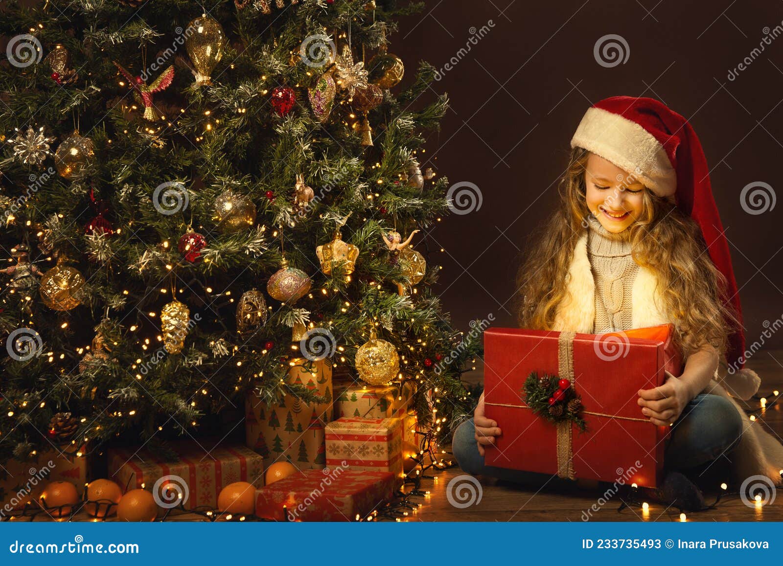 Petite Fille De Noël Dans Un Chapeau Santa Regarde Dans Une Boîte