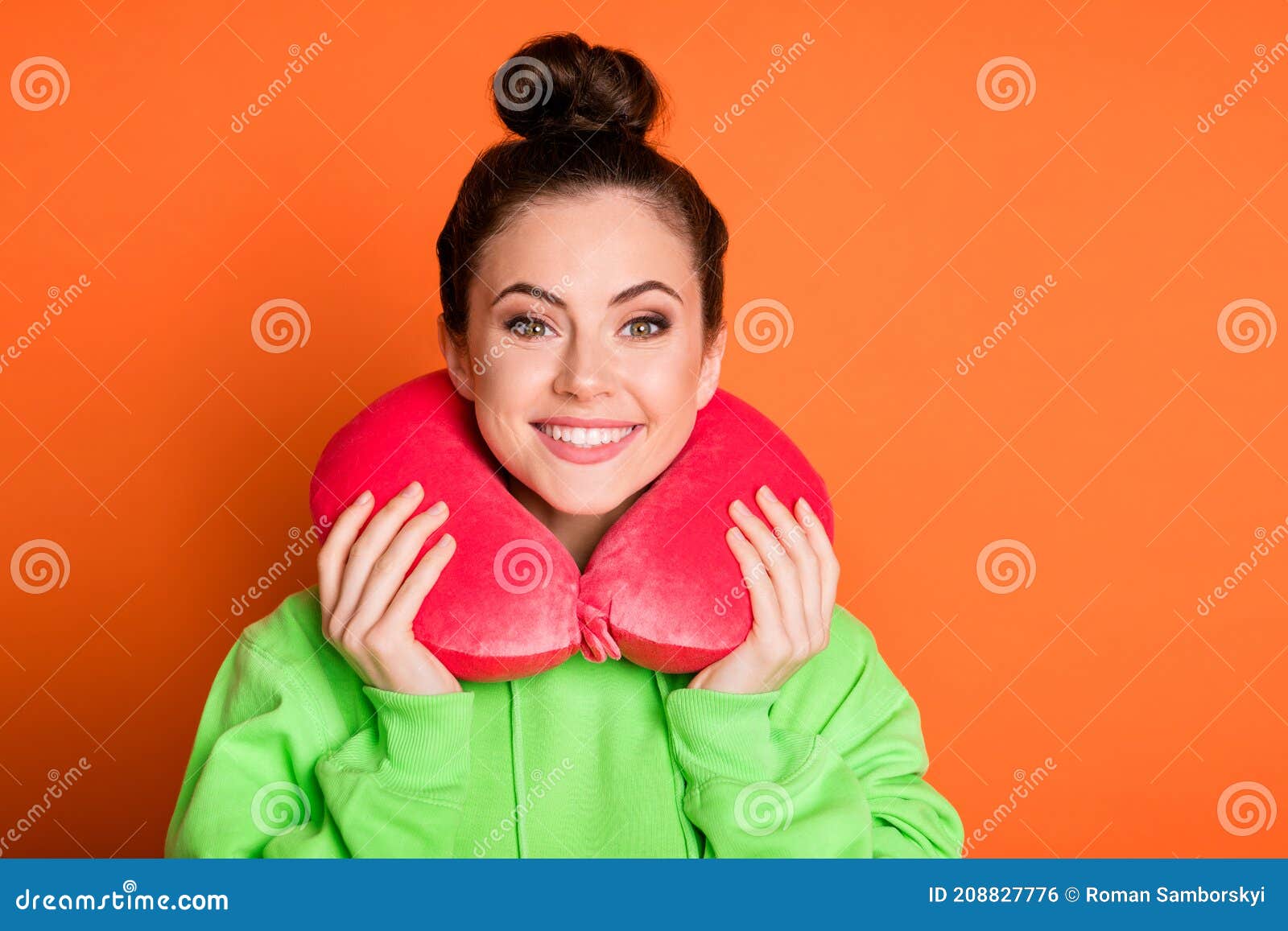 Photo of adorable young woman wear green hoodie neck pillow smiling isolated vivid orange color background.