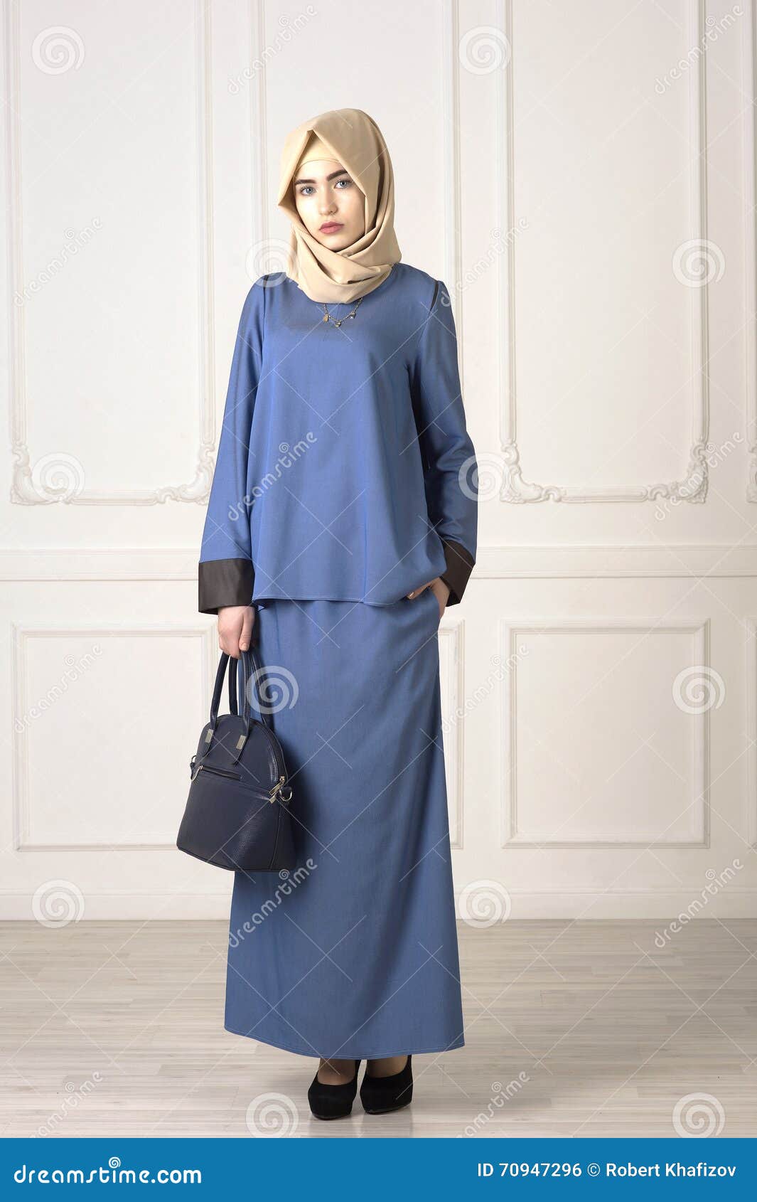 Photo of a beautiful woman in the modern Muslim clothes with bag and scarf on the classic light background, Ufa