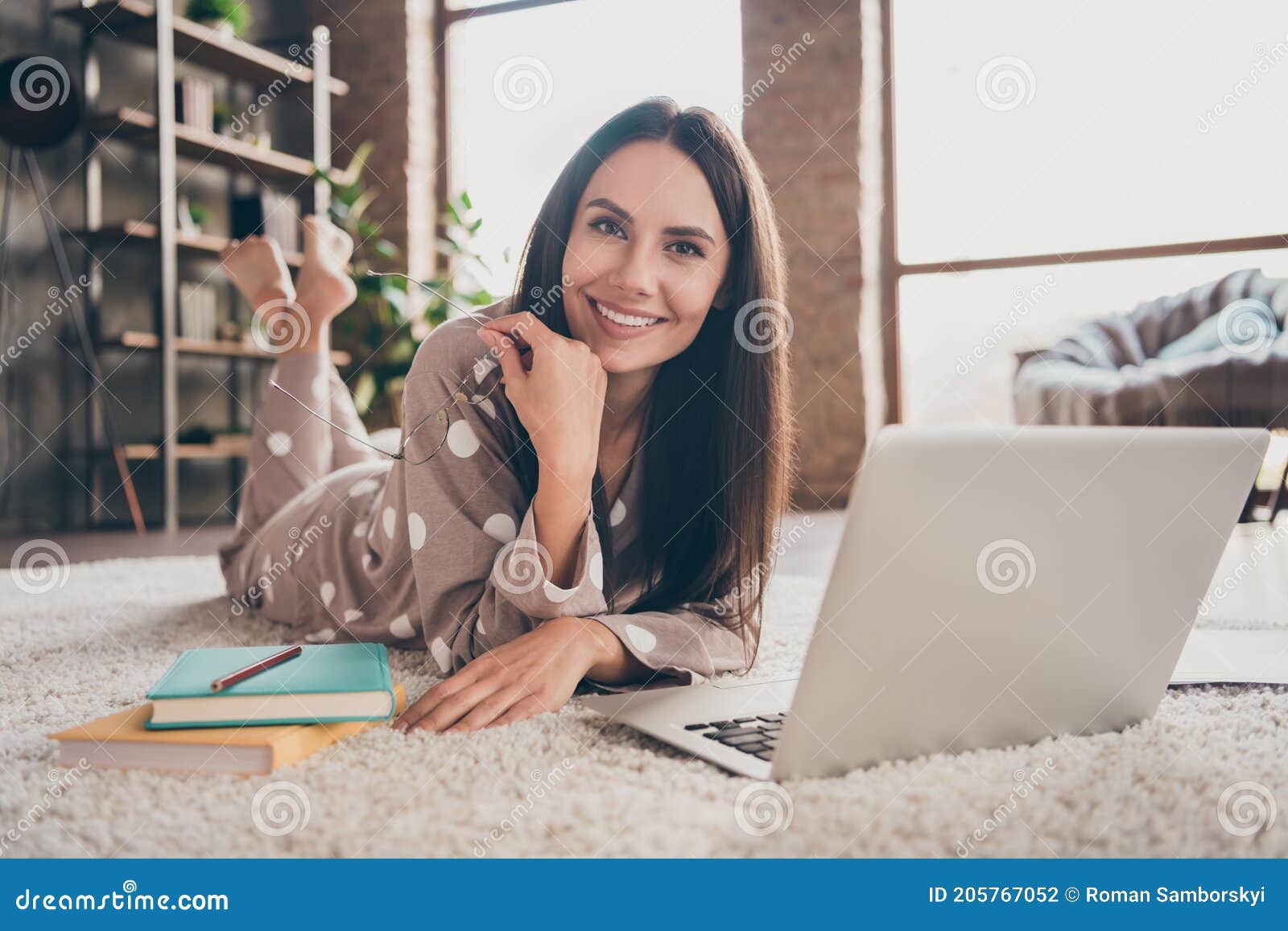 photo of cute optimistic girl lying on carpet take off spectacles wear pijama at home