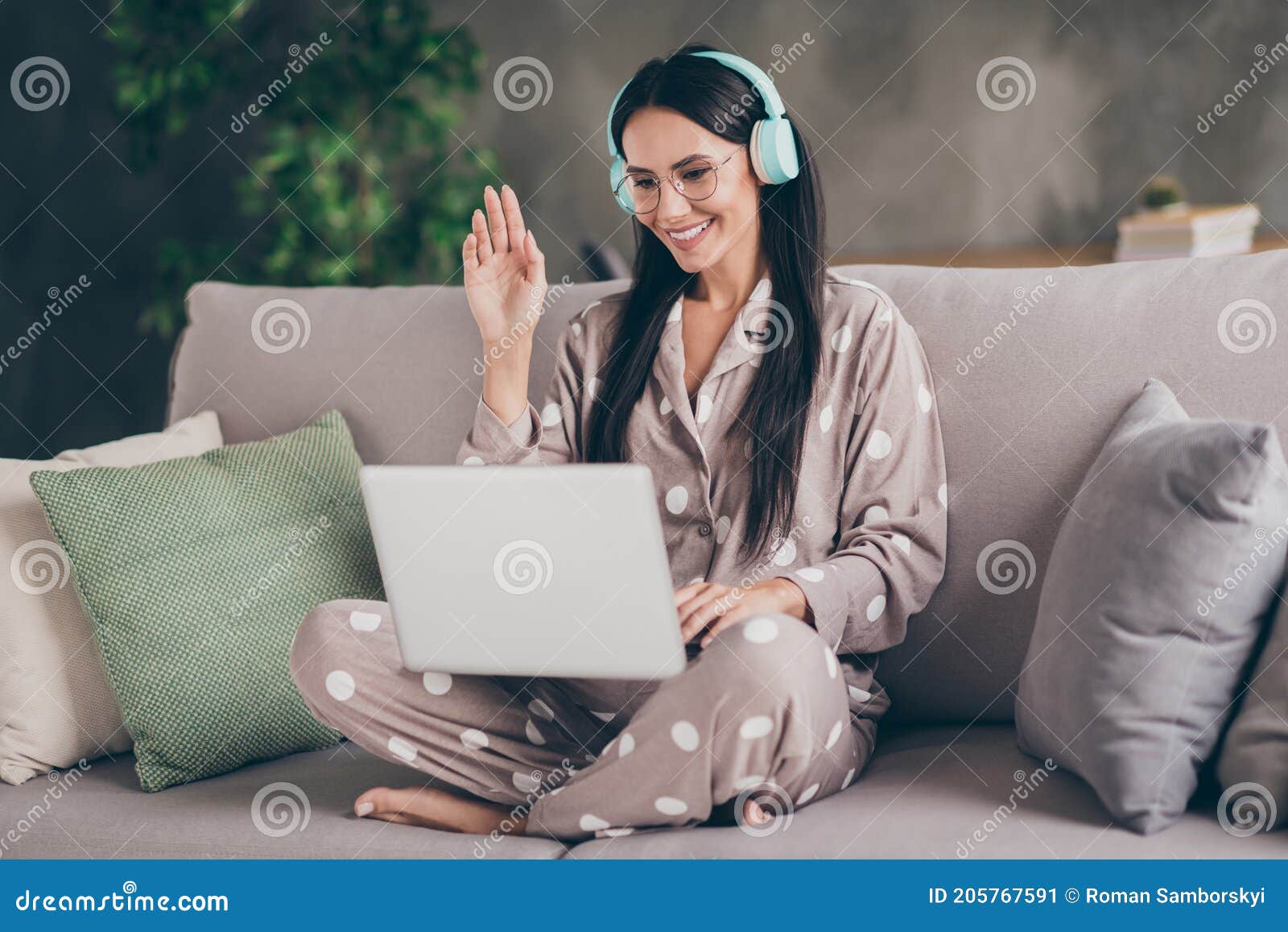 photo of nice optimistic girl sit talk laptop wave hand wear spectacles headphones pijama at home