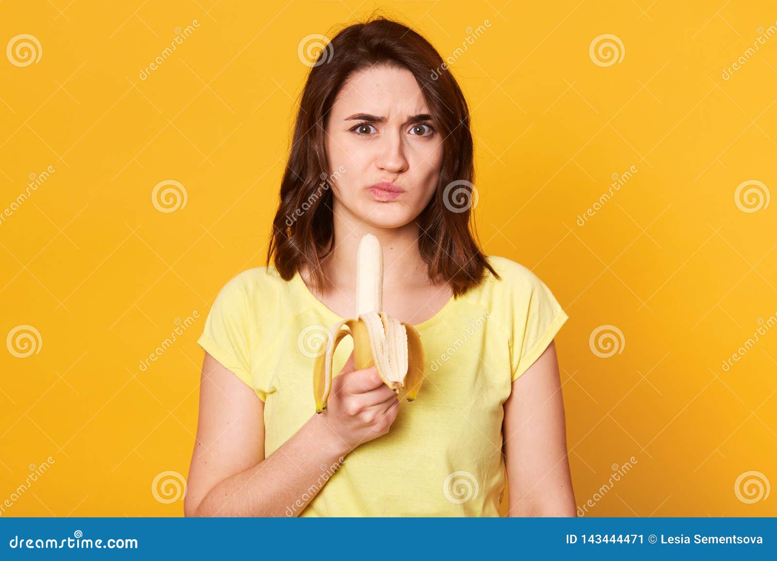 photo of pleasant looking woman in casual clothes, ready for eating fresh banana, does not like this fruit, has unpleasent facial