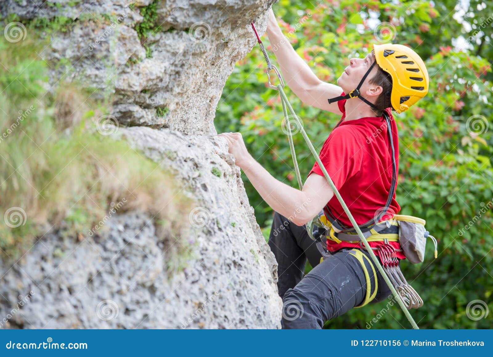 photo of sports man in helmet clambering over rock against background of green trees