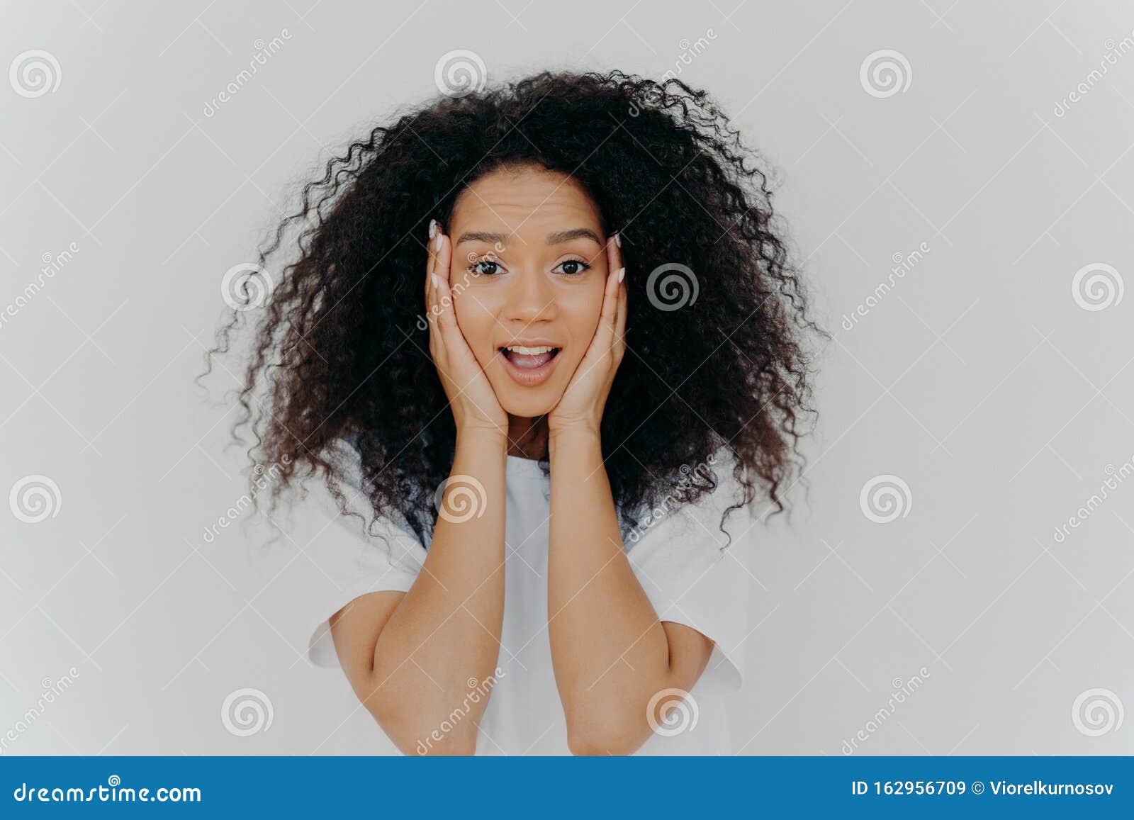 Photo Of Surprised Cheerful Woman With Afro Haircut Keeps Both Hands On Cheeks Has Natural