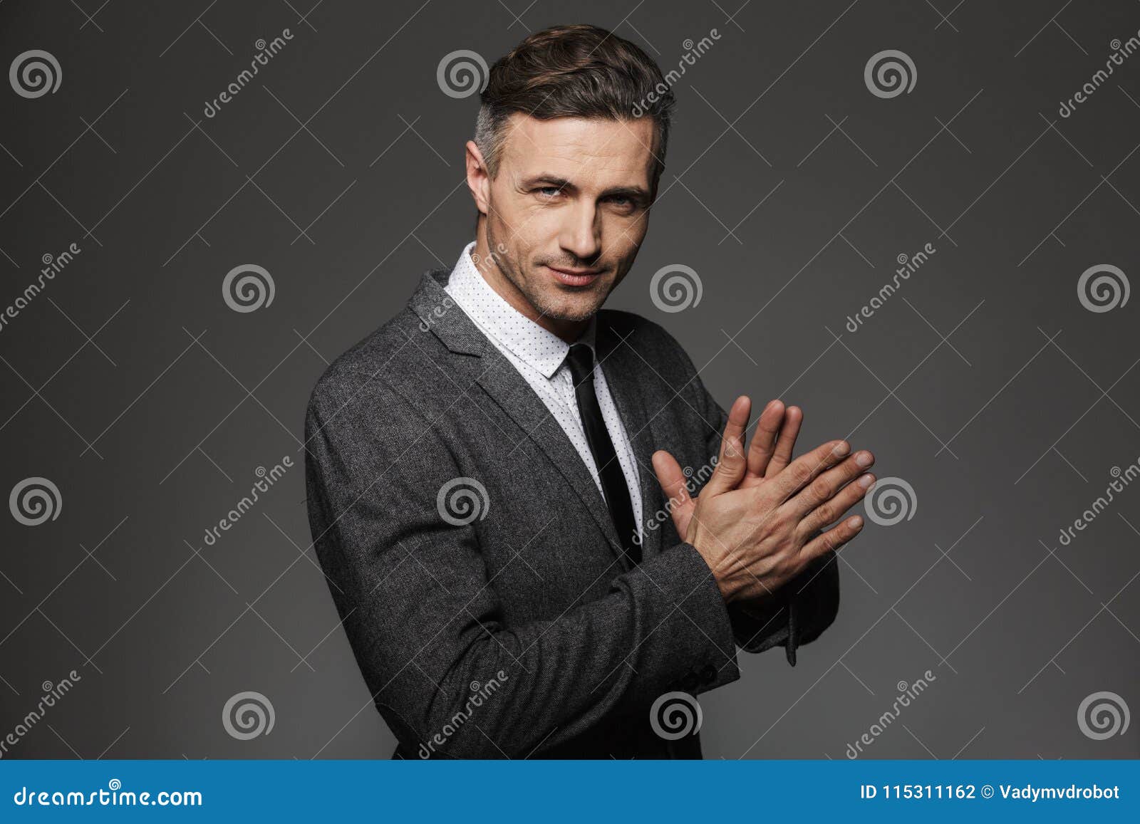 photo of unshaved successful man 30s wearing office suit and black tie smiling on camera holding hands together,  over gr