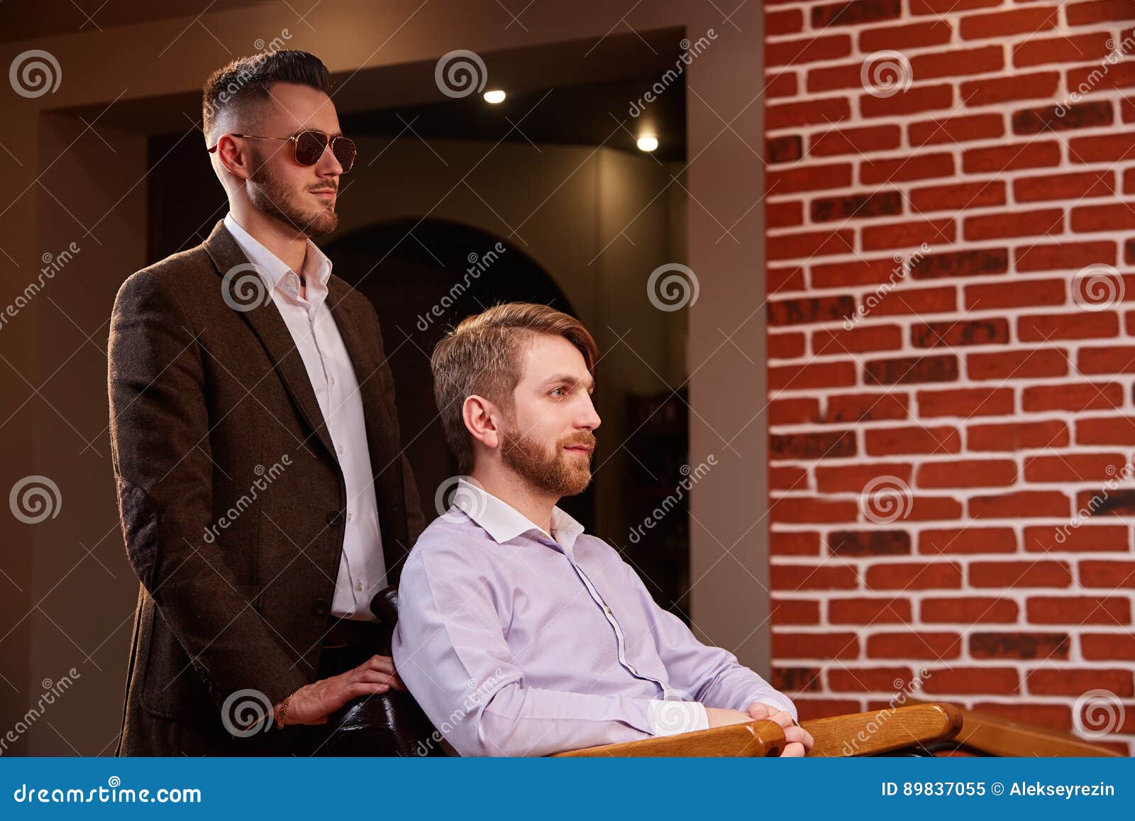 photo of young handsome man who sitting in chair at barbershop with hairdresses who standing by the armchair
