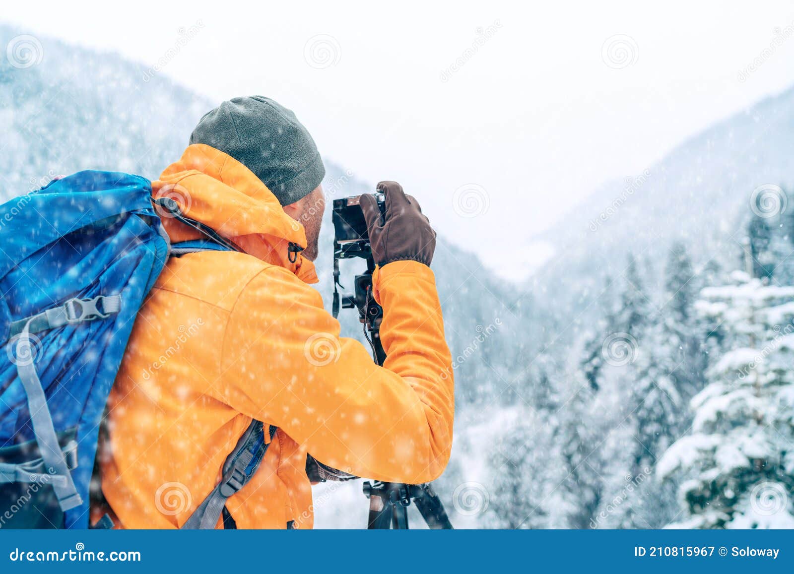 photographer dressed orange softshell jacket with backpack making a landscape shoot using a digital camera and tripod while he