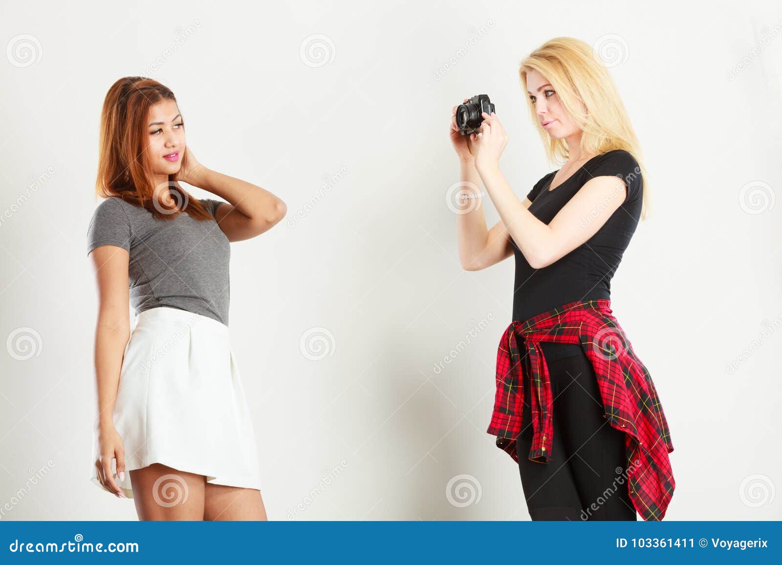 Blonde girl photographing mulatto woman. Photographer and model. Blonde girl shooting images, taking photos with camera, photographing mulatto female model