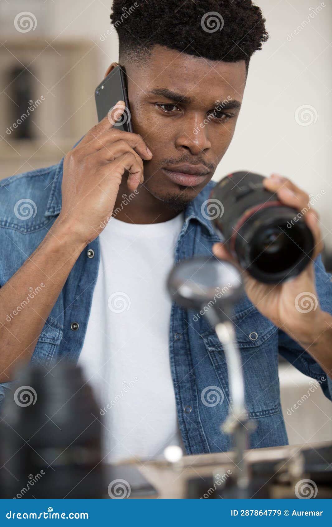 photography technician examining camera lens and talking on smartphone