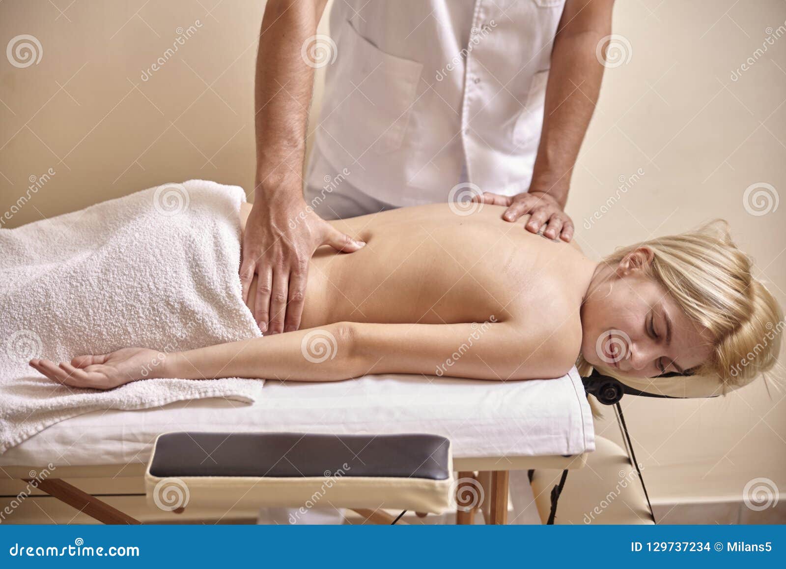 Hands of female therapist giving back massage to woman relaxing on