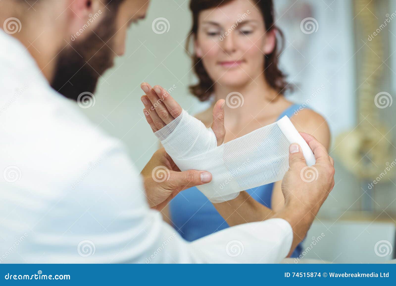 physiotherapist putting bandage on injured hand of patient