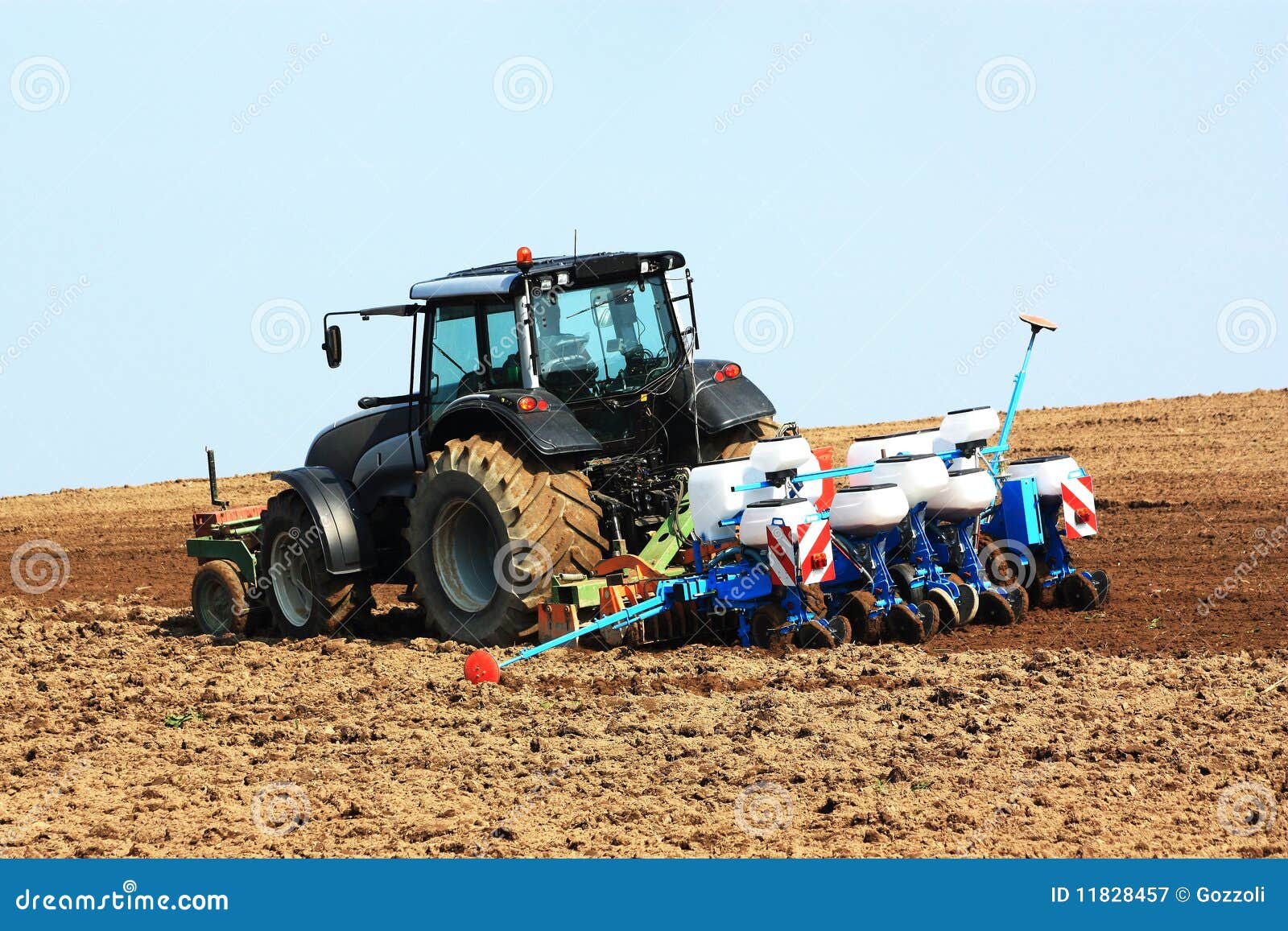 Piantatura del raccolto. Un coltivatore utilizza un trattore con un'unità di lavorazione e di piantatura per piantare il raccolto di estate in un campo recentemente arato.