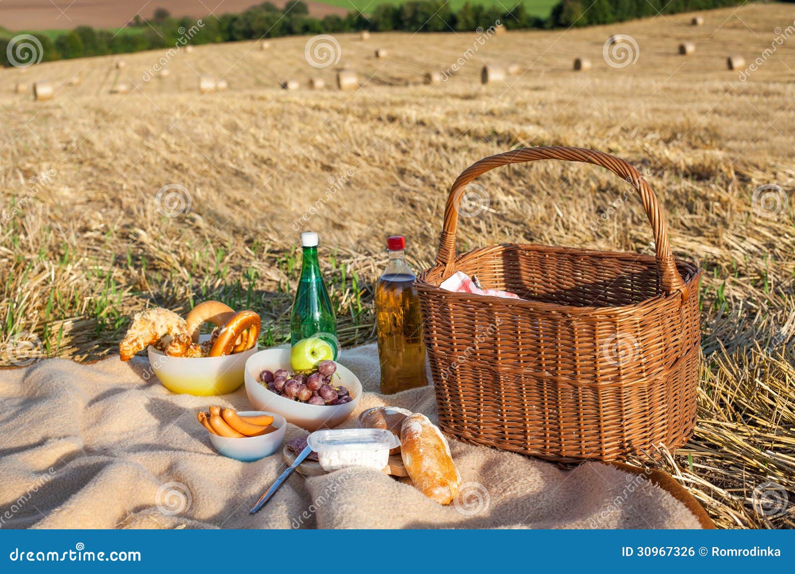 Picnic Basket and Different Food and Drinks on Straw Field Stock Photo