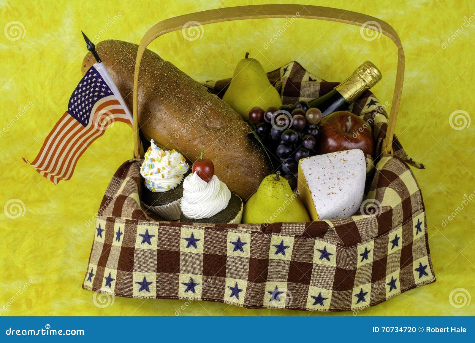 Picnic basket with fruit cheese bread wine cupcakes and American flag on yellow background