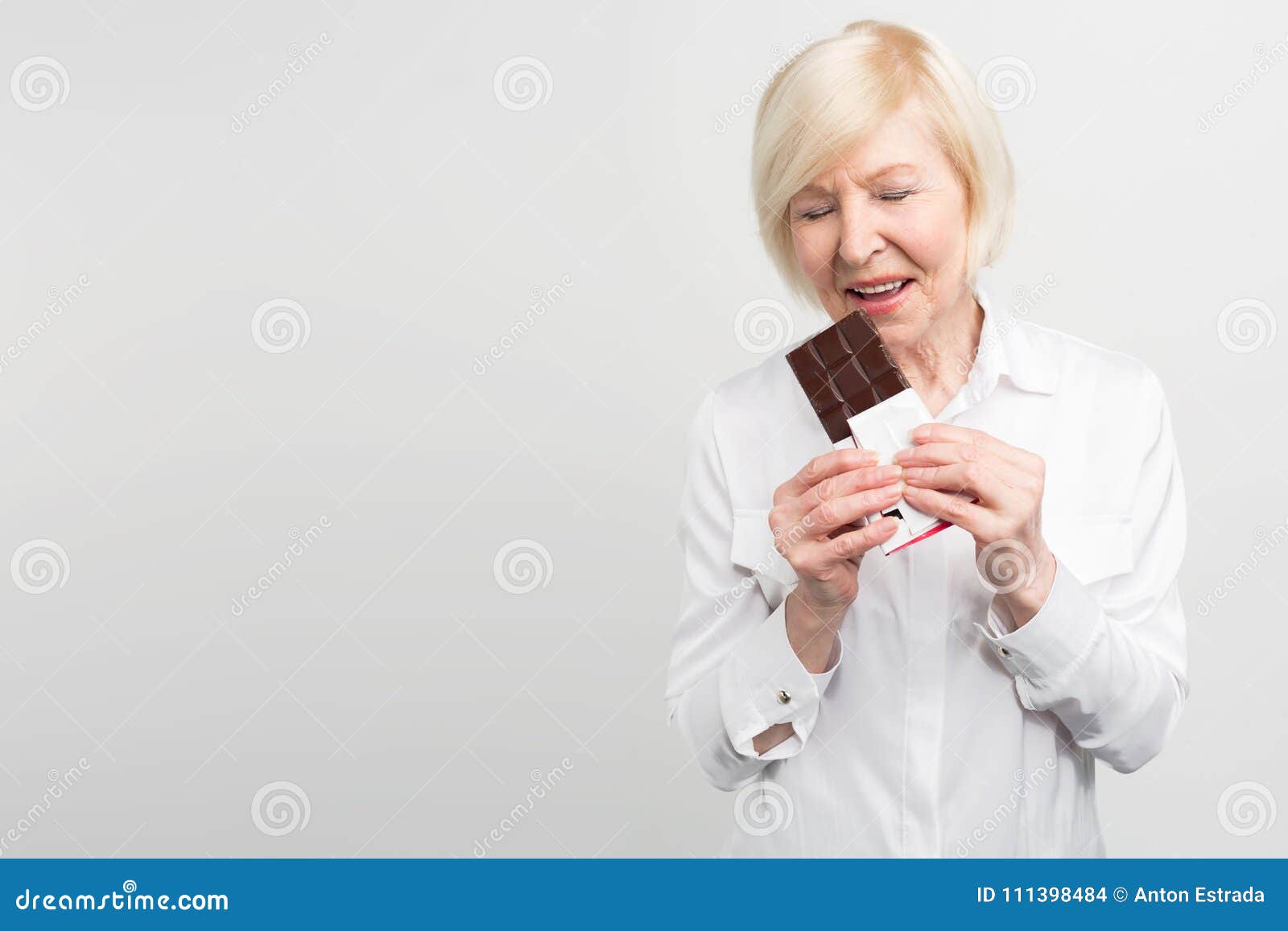 a picture of mautre lady eading a bar of milk chocolate. she likes to eat sweets. she cares about her health a lot but