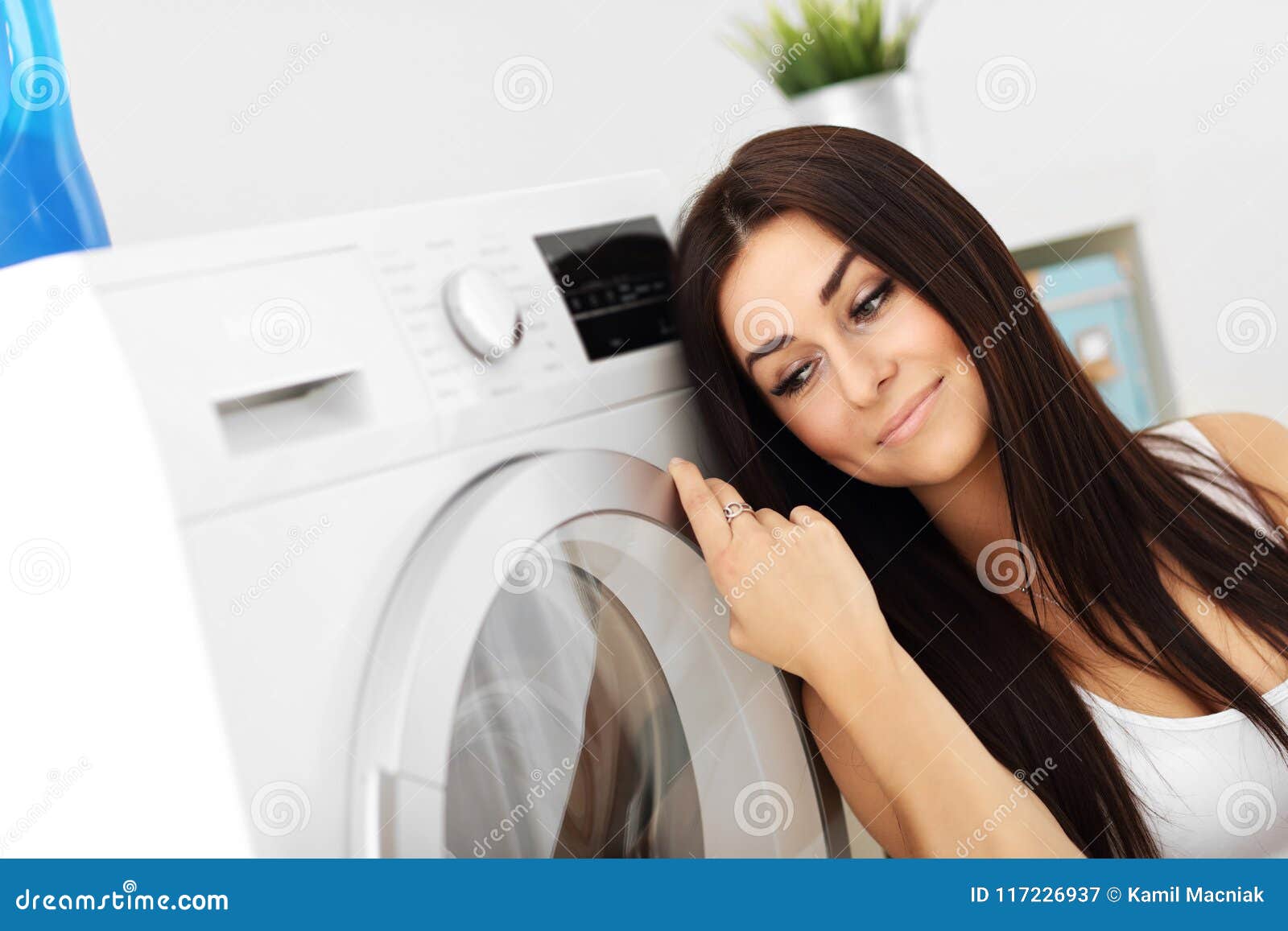 Portrait Of Young Housewife With Laundry Next To Washing Mach