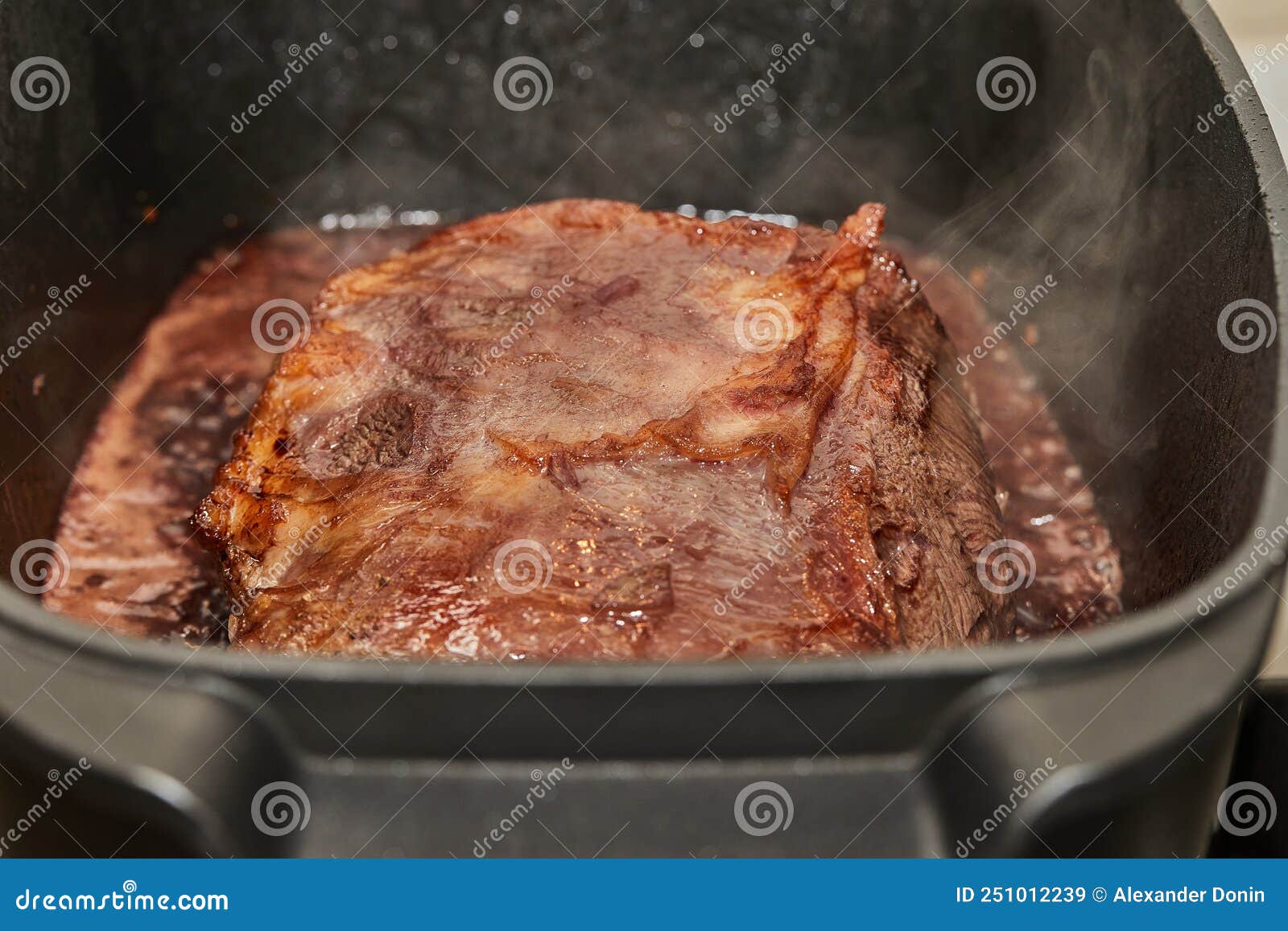Piece of Meat is Fried with Onions in Wine Sauce in Rectangular Pan Over Fire on Gas Stove Stock