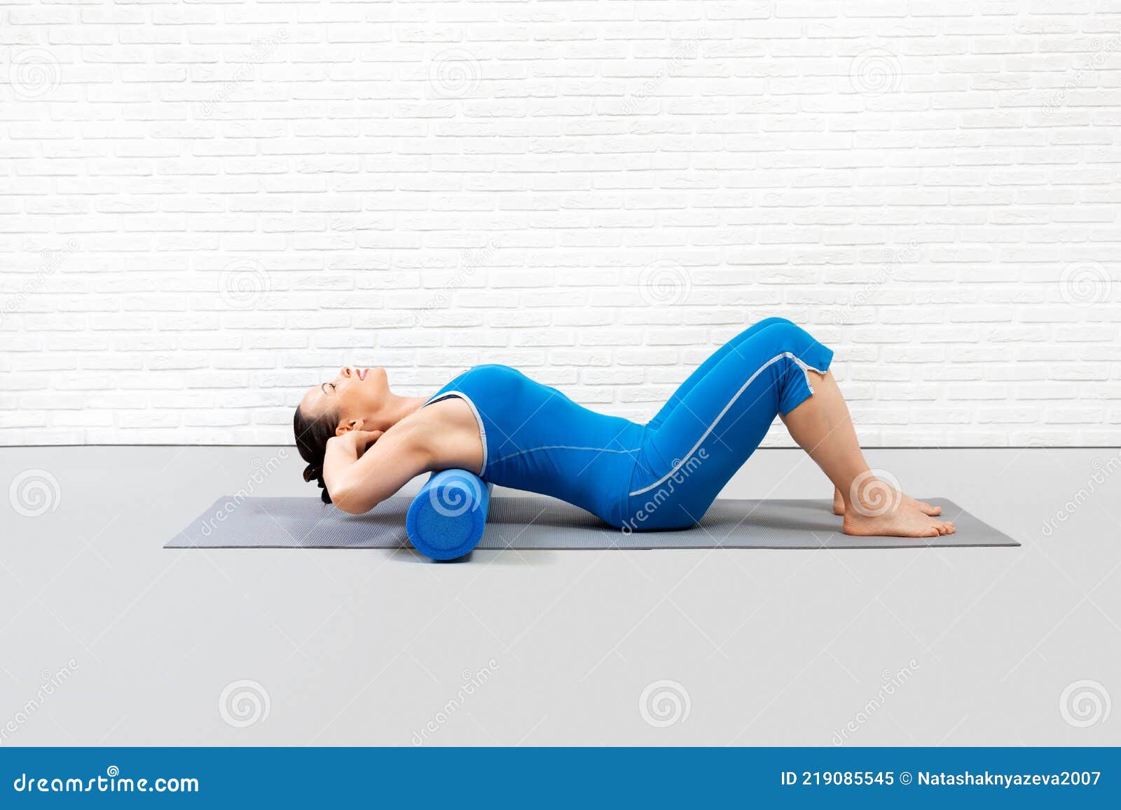 pilates with props indoor. adult caucasian woman in blue sportswear lies on a foam roller on the mat and stretching her