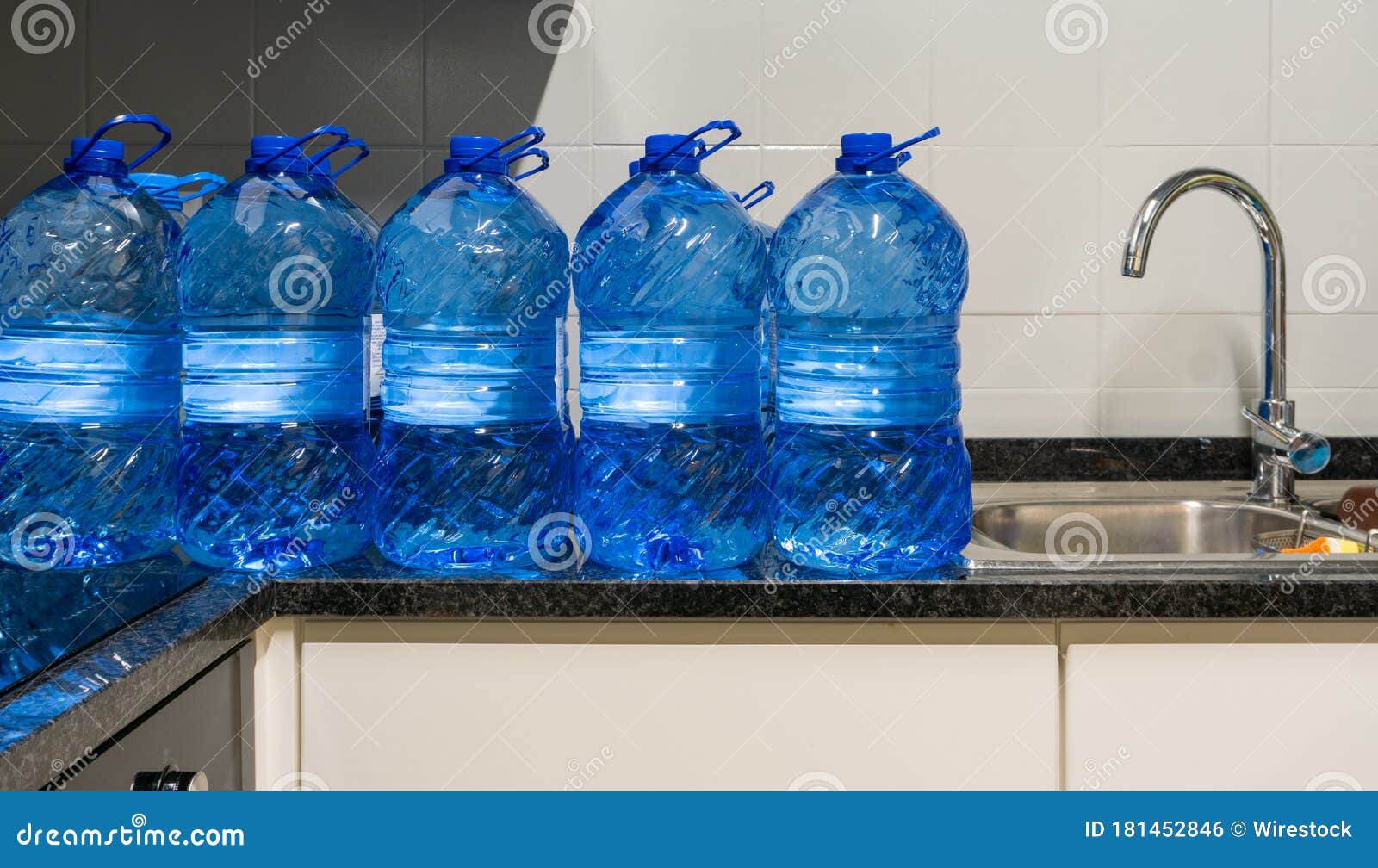 Pile of Gallons of Water beside a Sink Inside a Whitetiled Kitchen