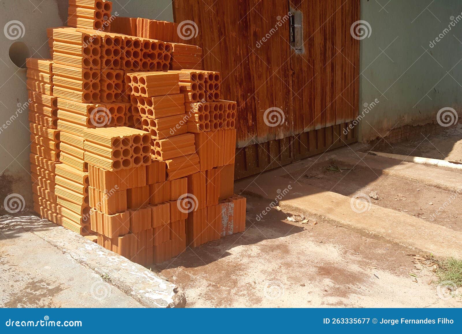 pile of six-hole bricks on the floor, leaning against the wall next to the rusty orange gate