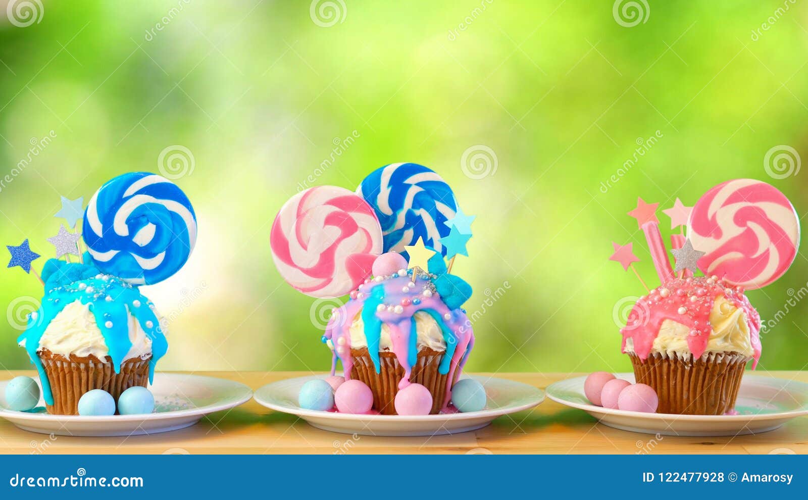 pink and blue novelty cupcakes decorated with lollipop against garden background