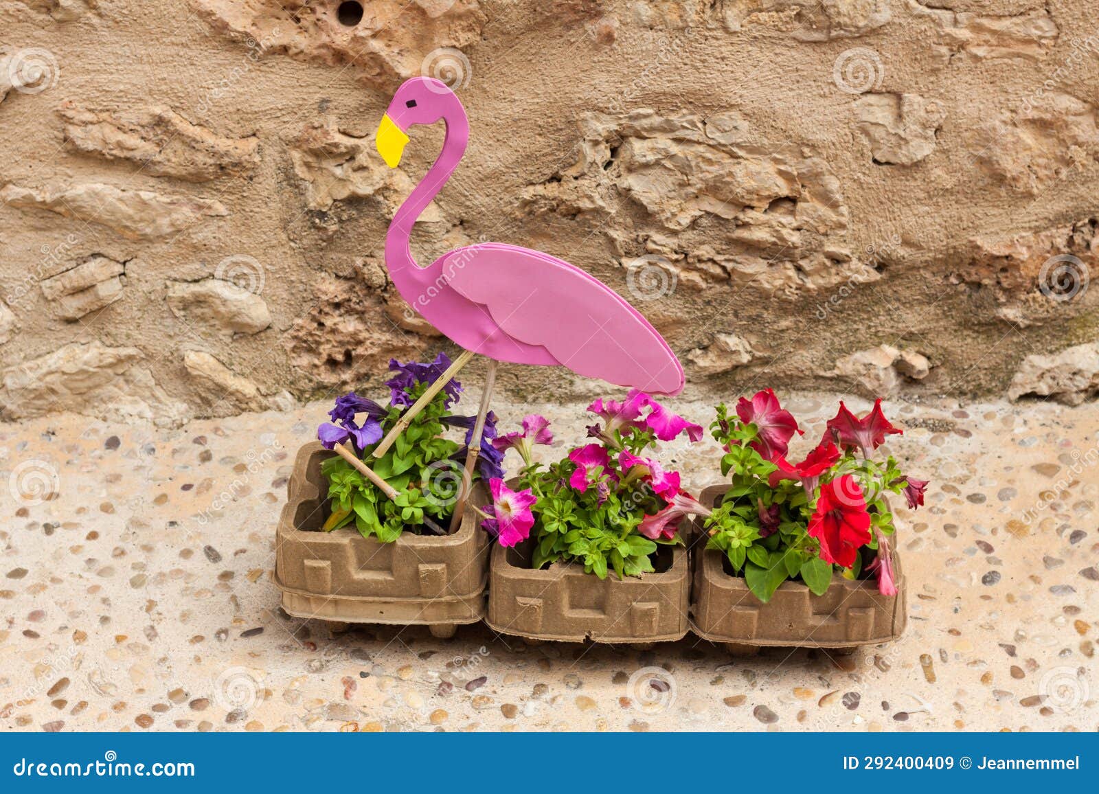 pink flamingo sitting in a flower pot with petunia flowers on 