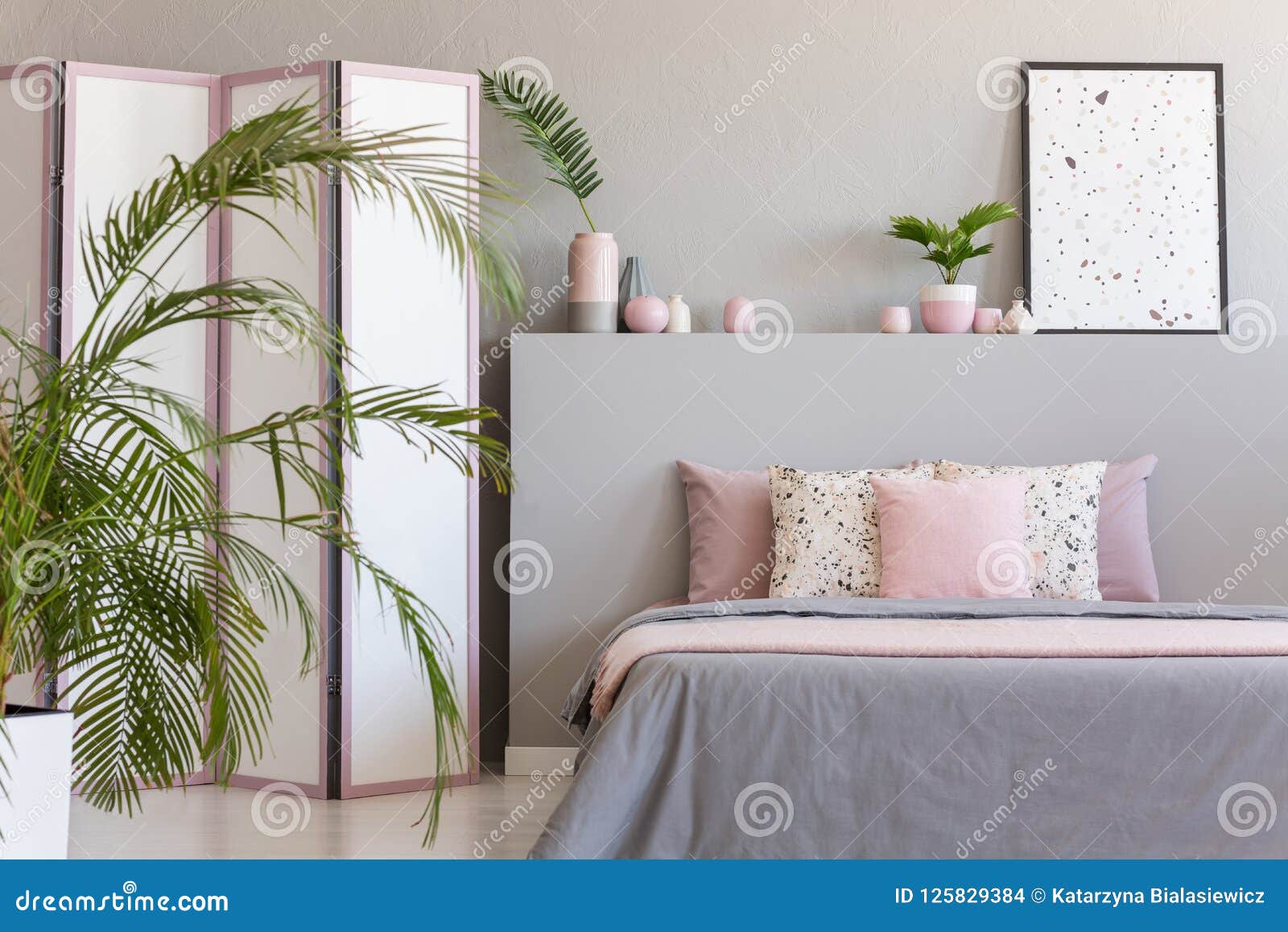 pink pillows on grey bed in pastel bedroom interior with palm and poster on bedhead. real photo