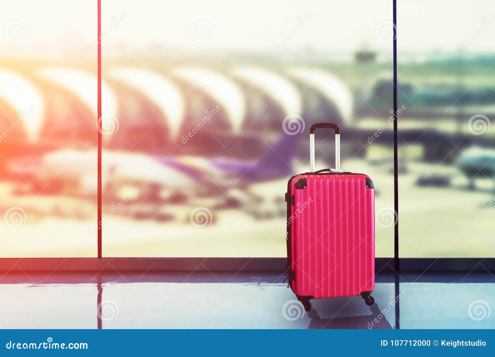 pink suitcases in airport departure lounge, airplane in background