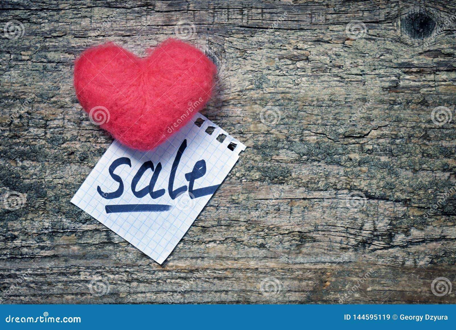 pink wool toy heart lying with a notepad sheet with a word sale written on it on a wooden desk