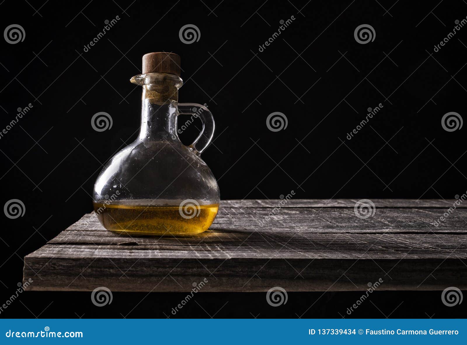 Pitcher of Olive Oil on Old Wood on Black Background Stock Photo