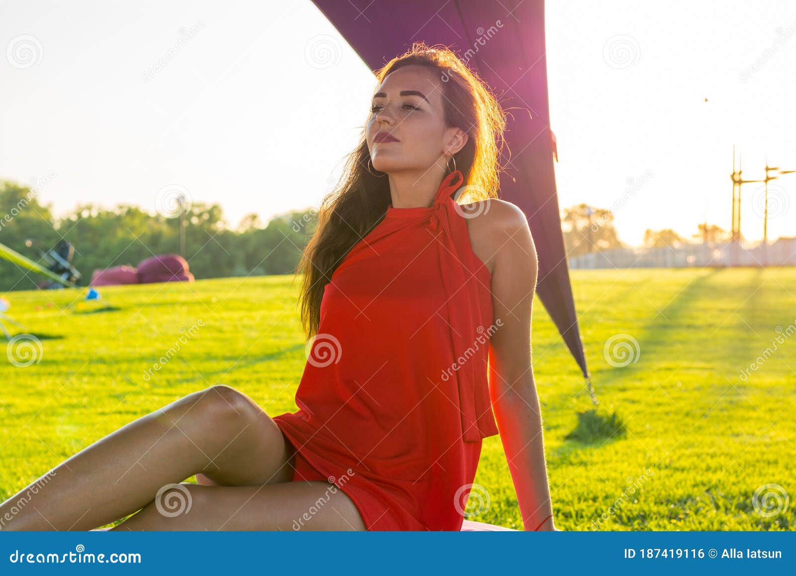 Piękna młoda brunetka z długimi włosami w czerwonej sukience na lounger w obszarze rekreacyjnym z namiotami o zachodzie słońca