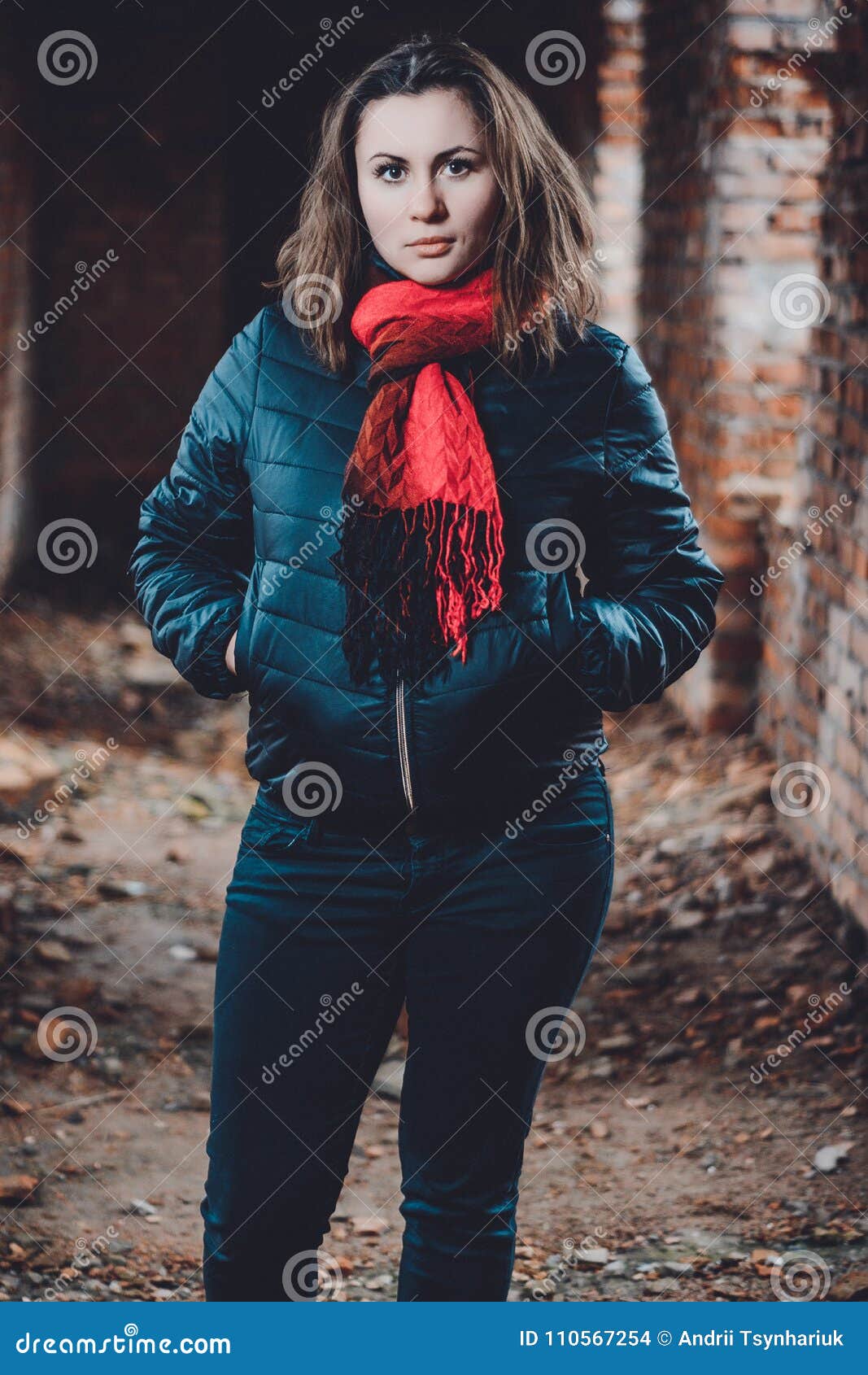 Piękna młodej kobiety pozycja w zniszczonym budynku w zimnym tonięciu. Fotografia młoda piękna dziewczyna w ruinach przeciw tłu ściana z cegieł w kurtce i spodniach W fotografii tam  jest zimny tonowanie