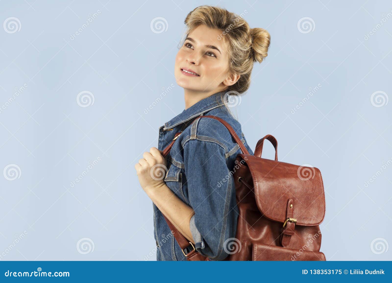 Szczęśliwa piękna studencka dziewczyna w drelichowej kurtce z plecakiem na ona ramiona w studiu na błękitnym tle Pojęcie edukacja i uczenie