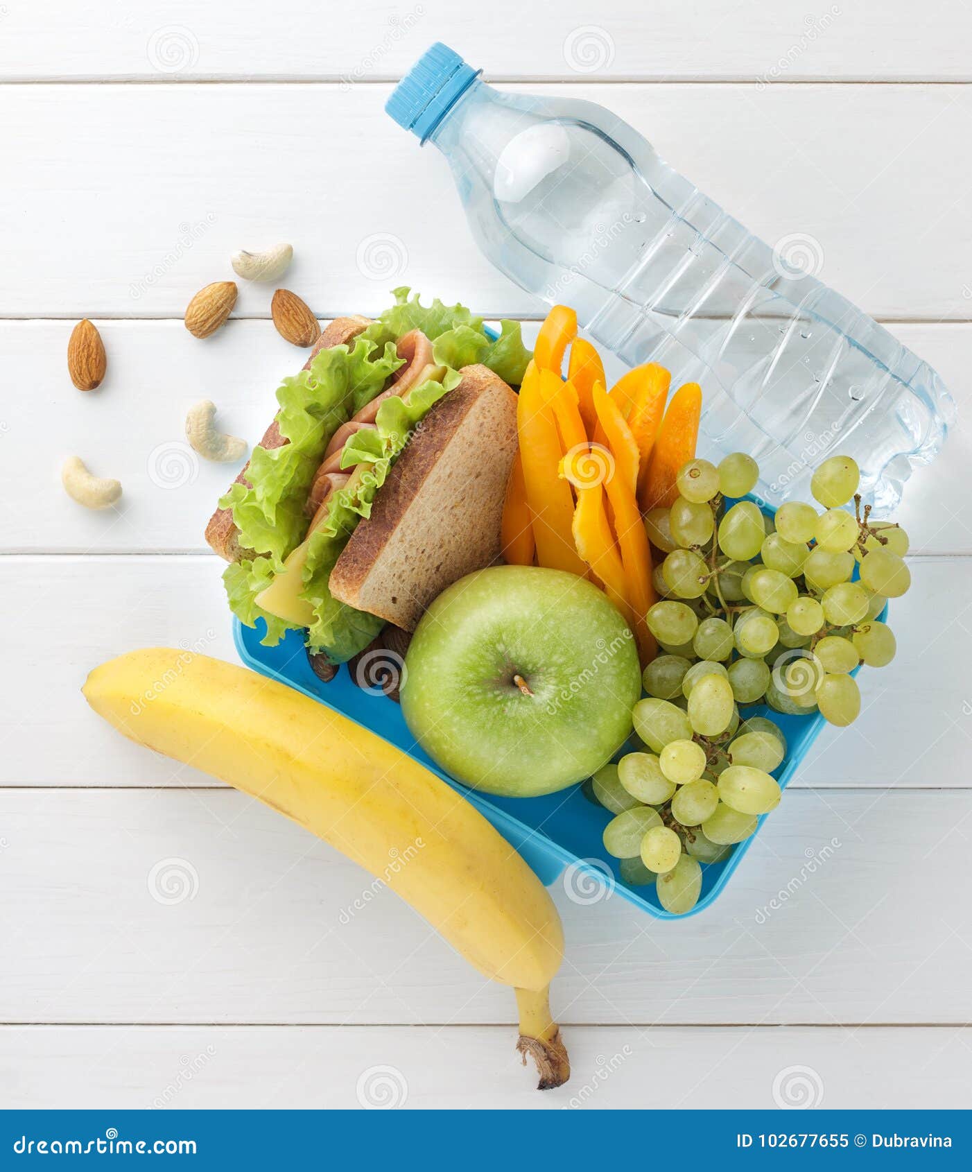 Plast- lunchask med smörgåsen, frukter, grönsaker, muttrar och vatten på den vita trätabellen Top beskådar